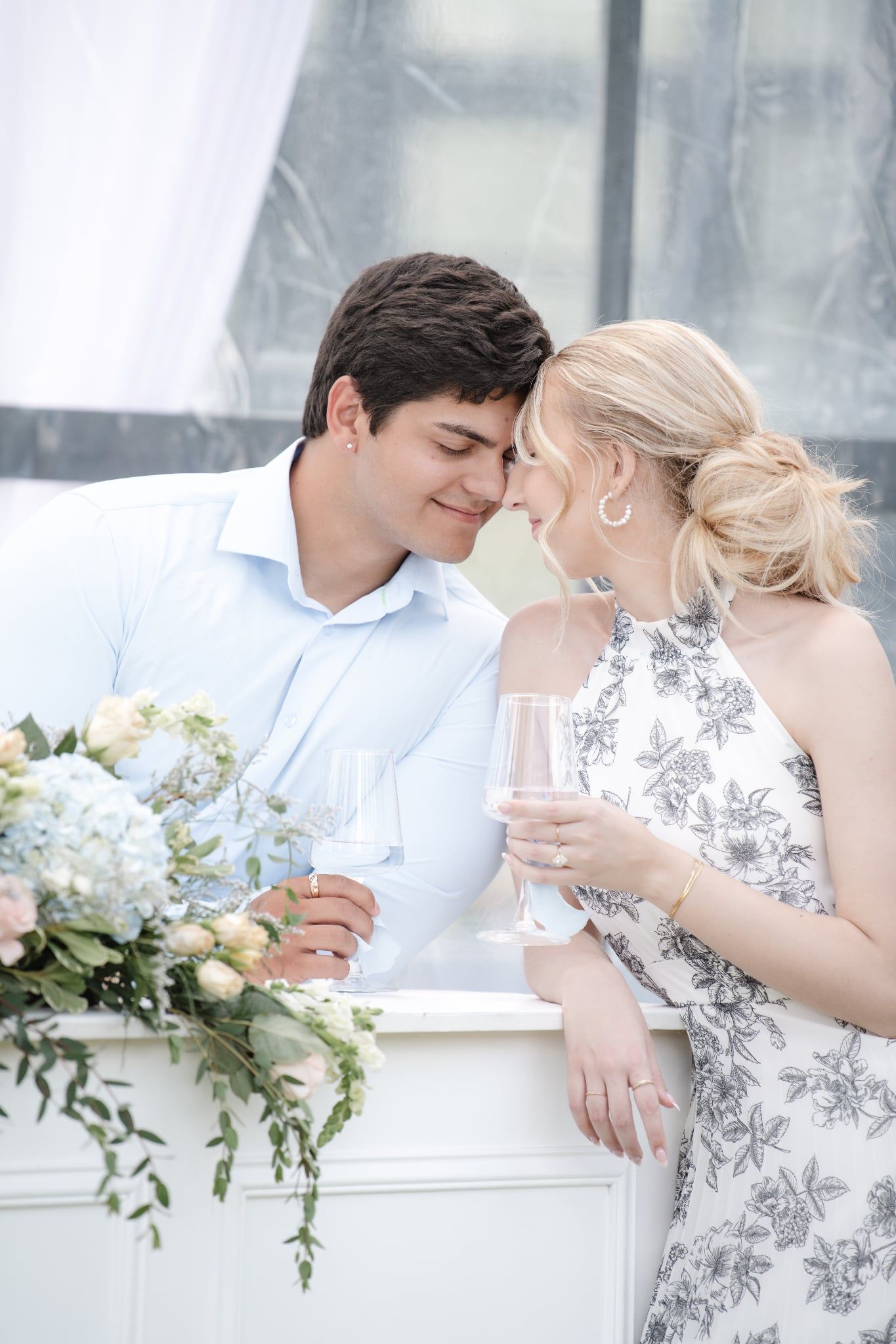 Romantic couple in formal attire share intimate moments against a light-filled backdrop with floral decorations.