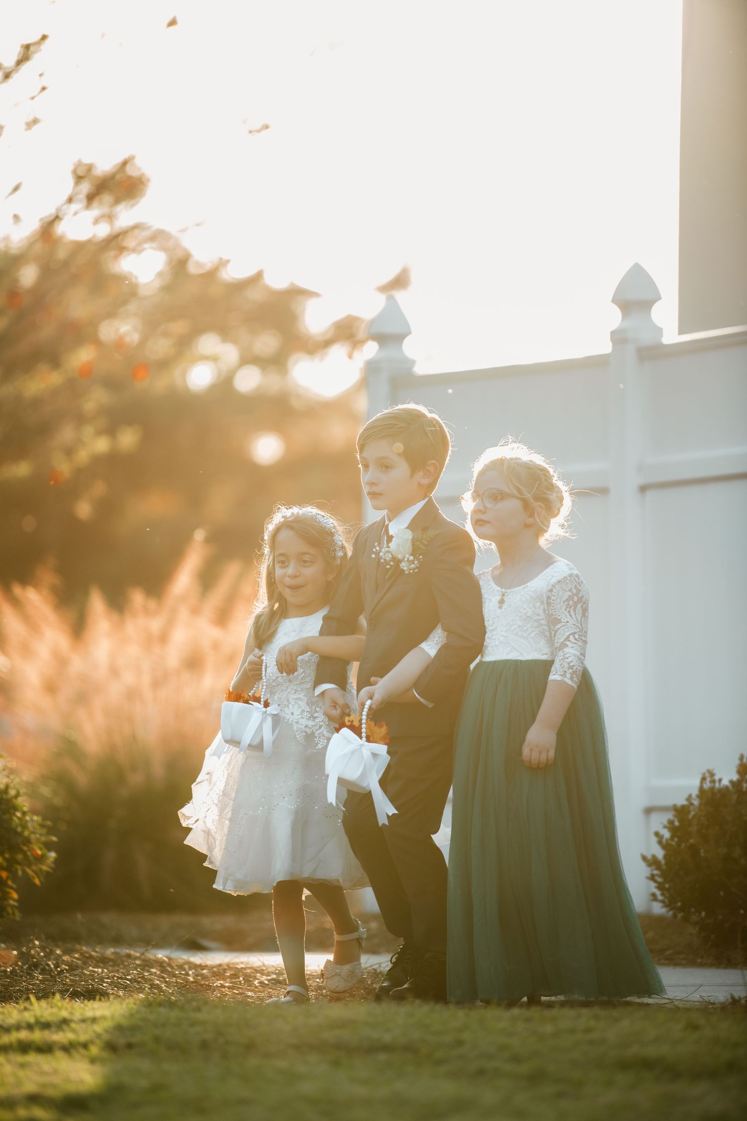 Wedding party poses in golden sunlight against white building backdrop.