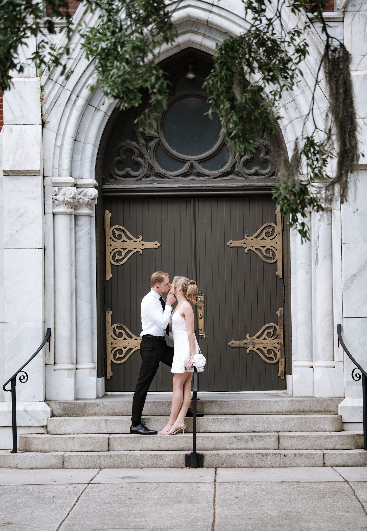 A couple embracing on church steps in front of an ornate gothic doorway.