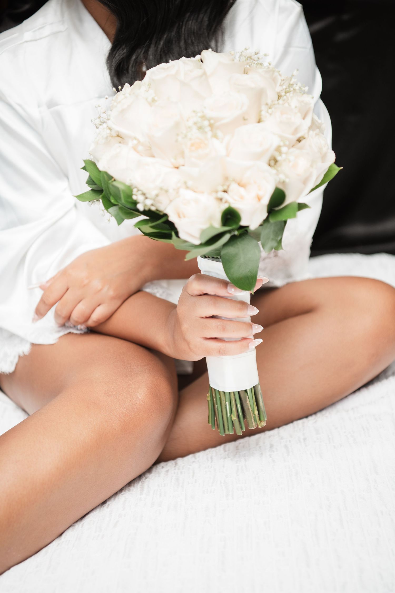 A white bridal bouquet rests elegantly on white fabric with delicate lace details.