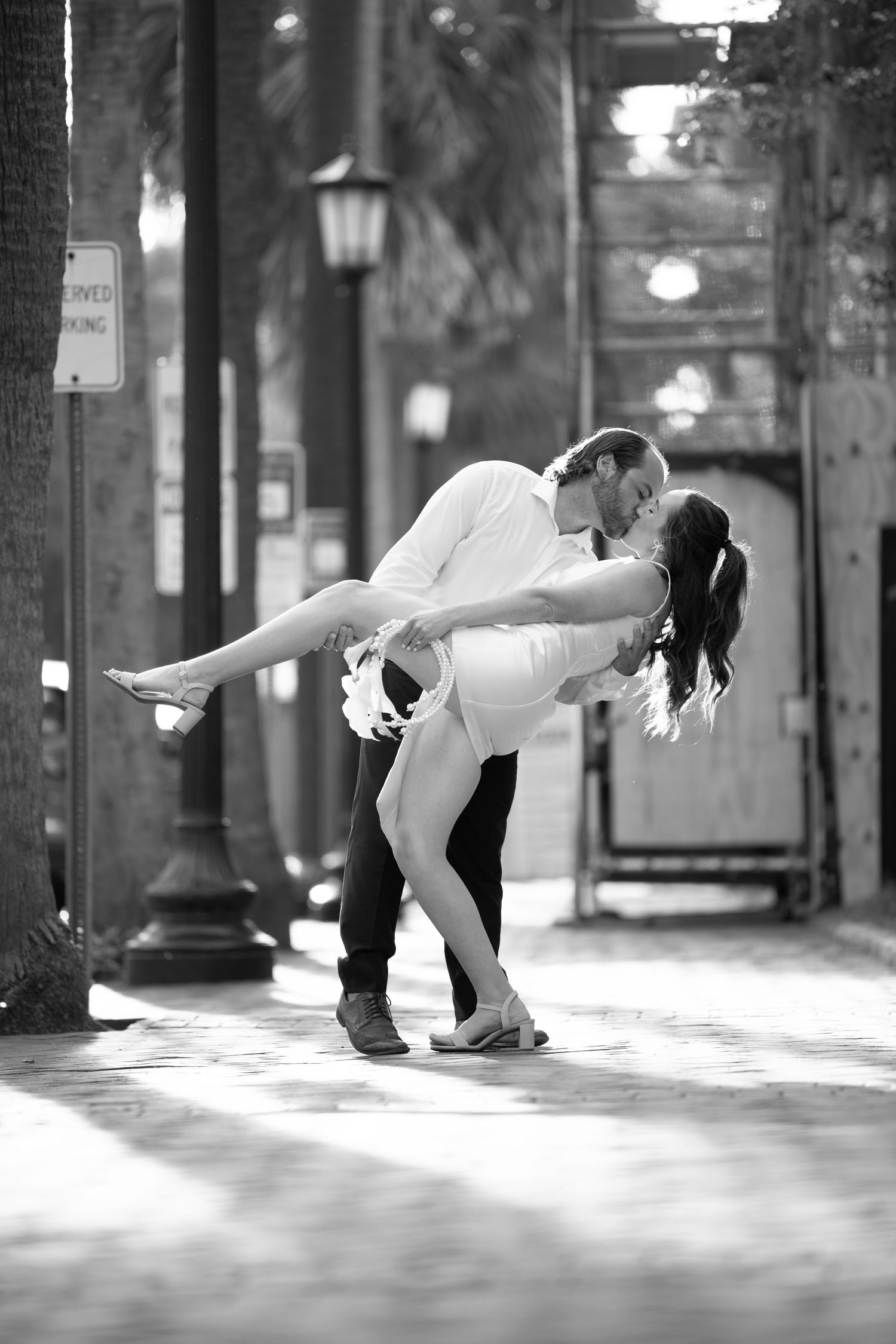 A romantic black and white photograph of a couple sharing an intimate dip pose on a lamp-lit city street.