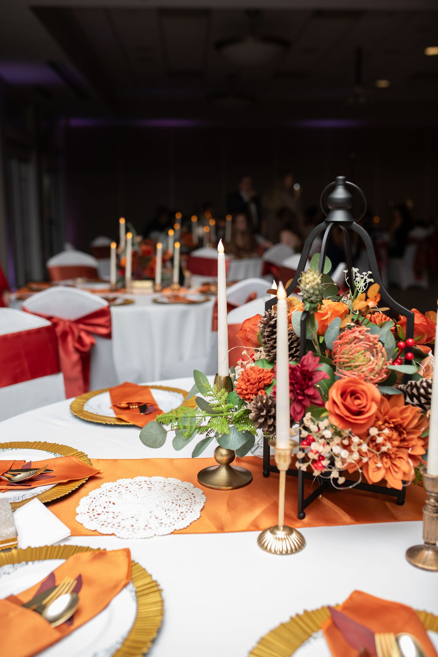 Wedding reception table decorated with orange roses, white candles and gold charger plates.