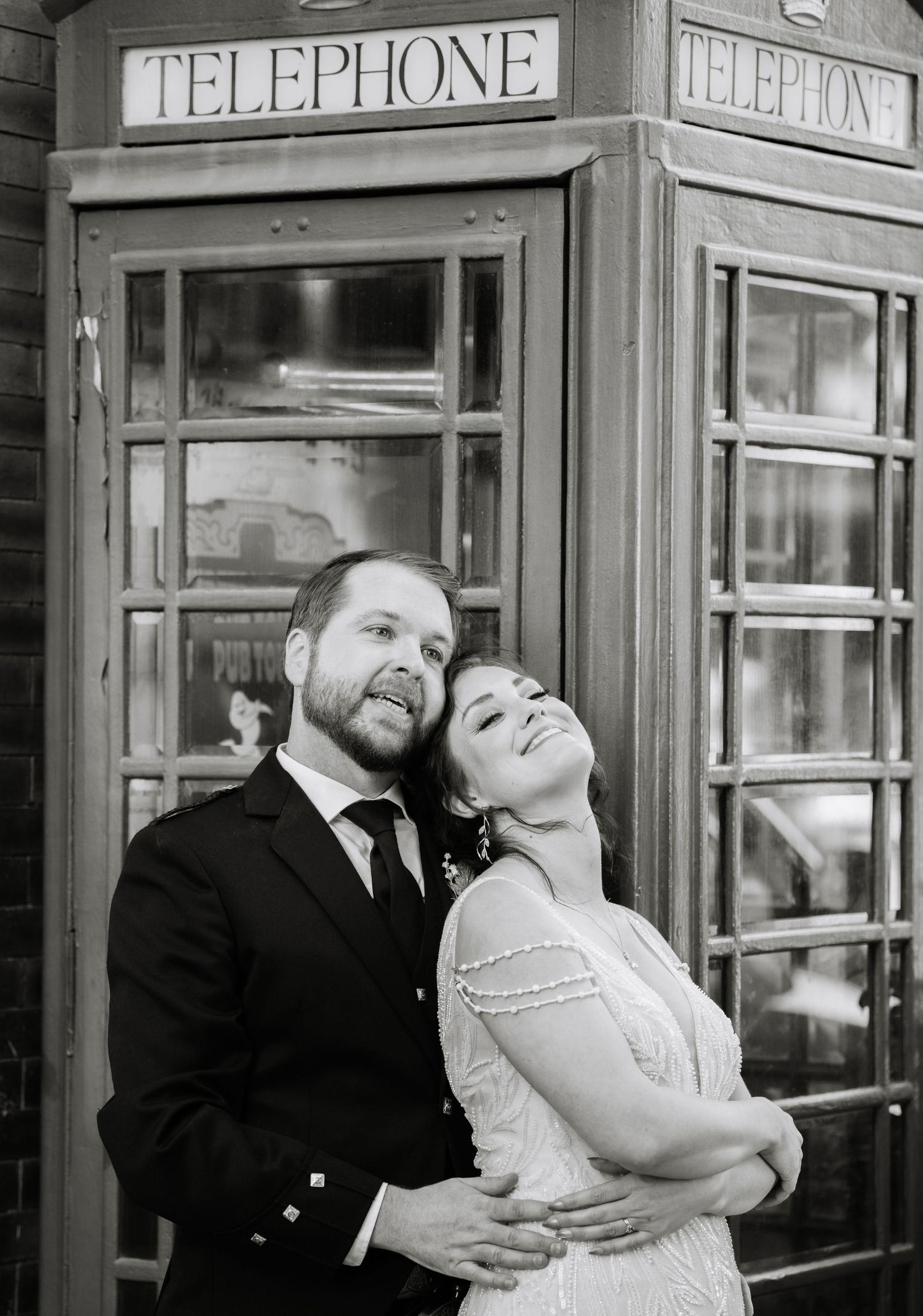 Black and white photo of a couple posing by vintage telephone booths.