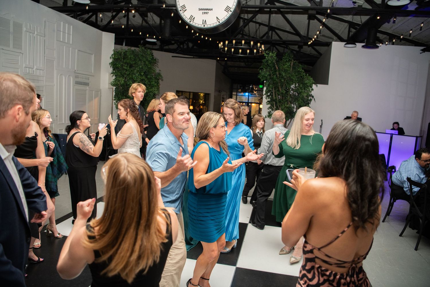 Wedding guests dancing and taking photos during reception celebration.