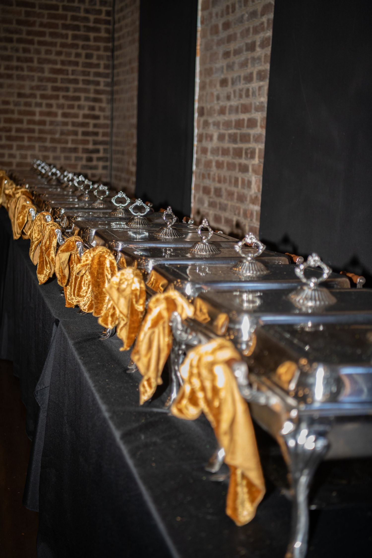 Formal dining setup with gold bow-tied chairs and silver serving dishes on black tablecloths.
