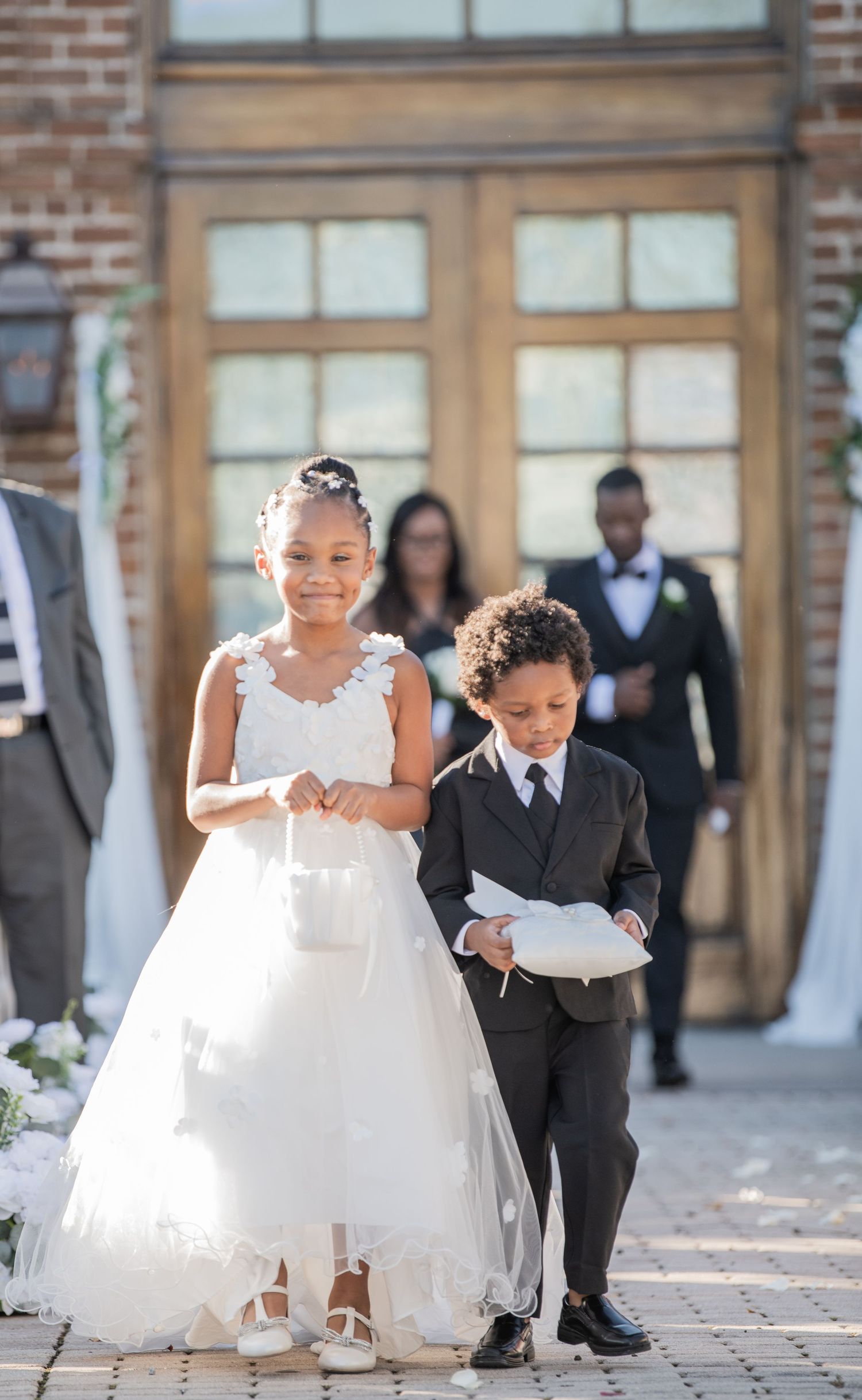 Children in formal attire walking down the aisle at an outdoor wedding ceremony.