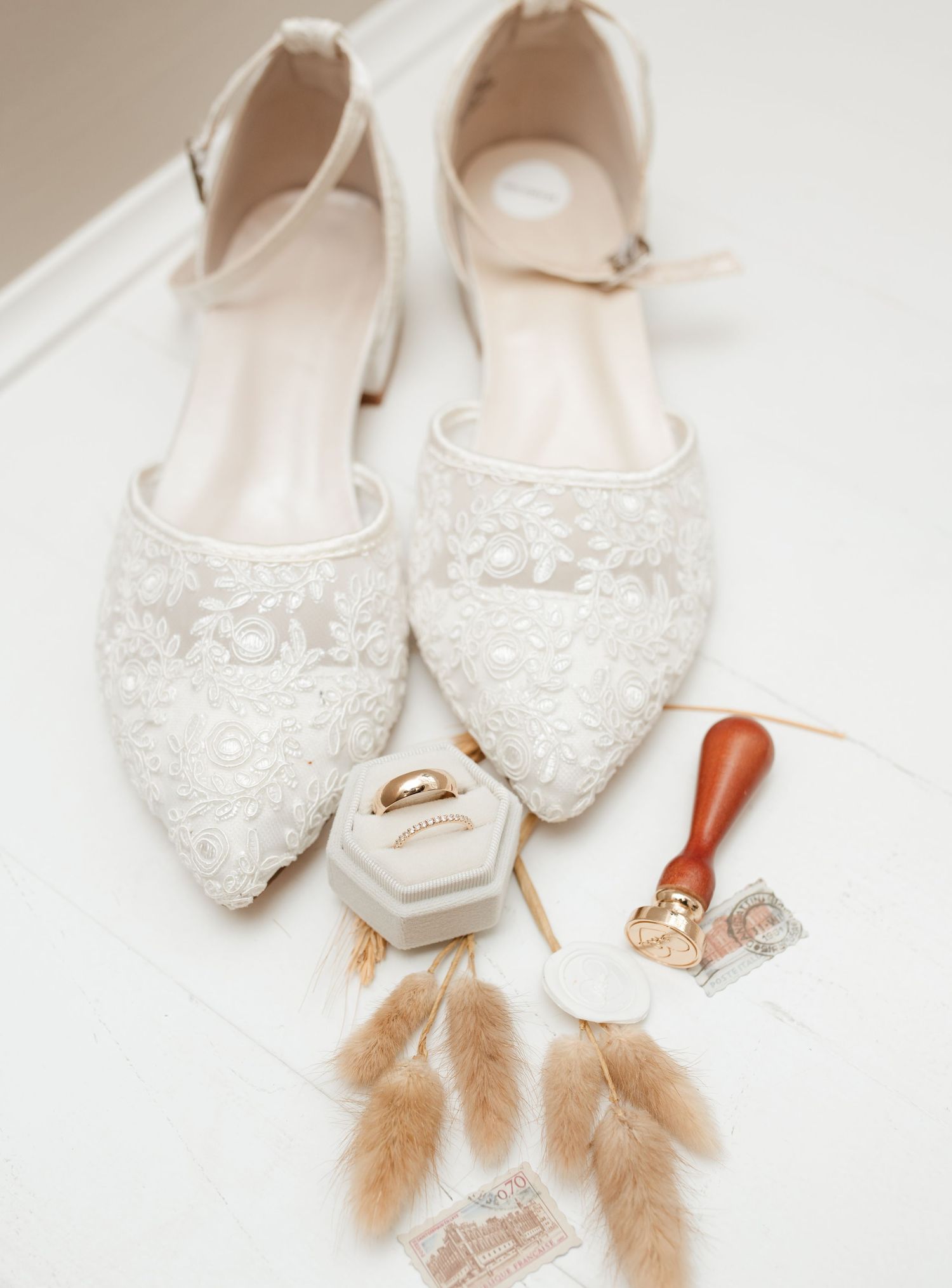 White lace bridal shoes with wedding rings and feather accessories.