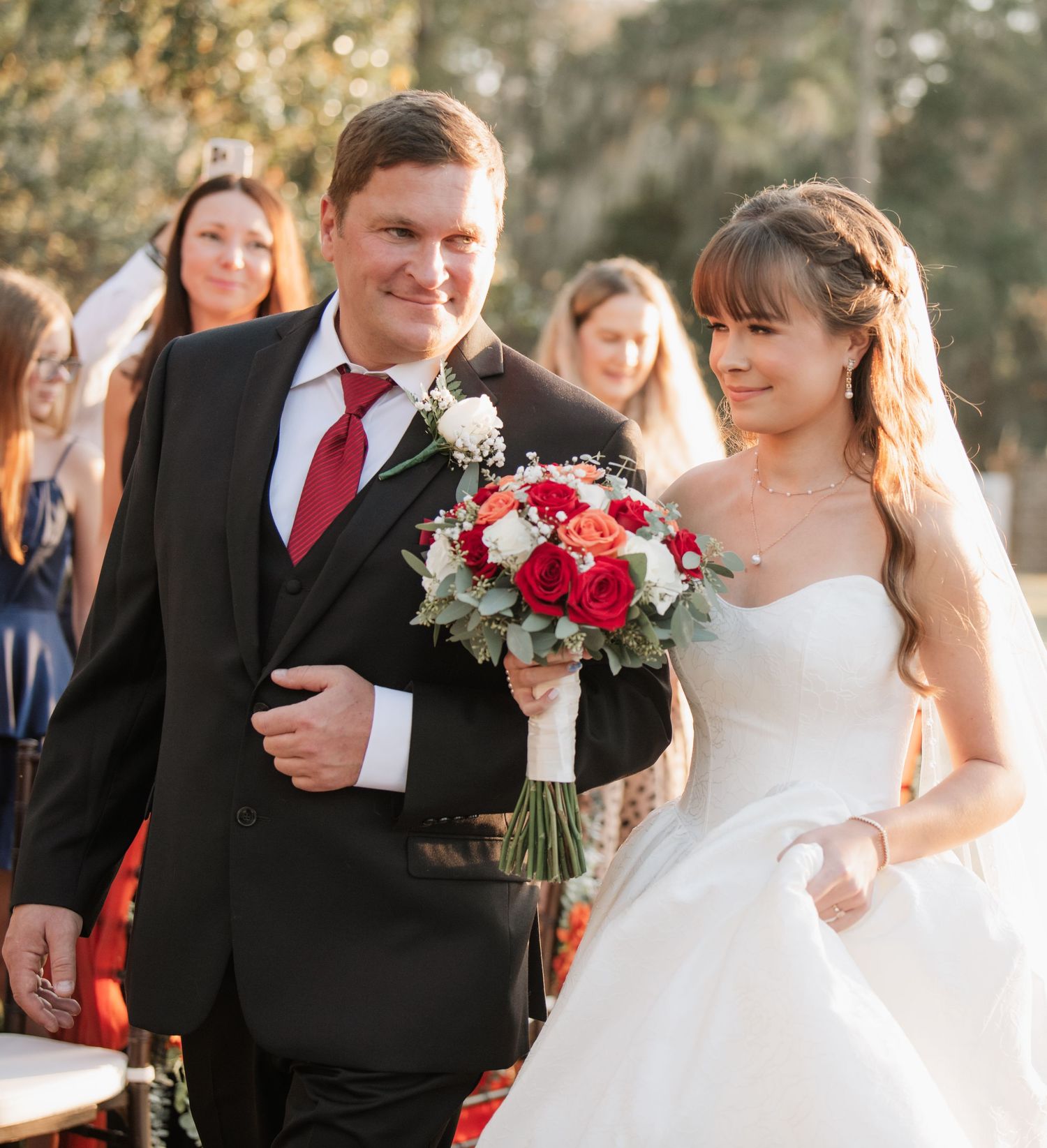 Wedding party poses outdoors with red and white floral bouquets.