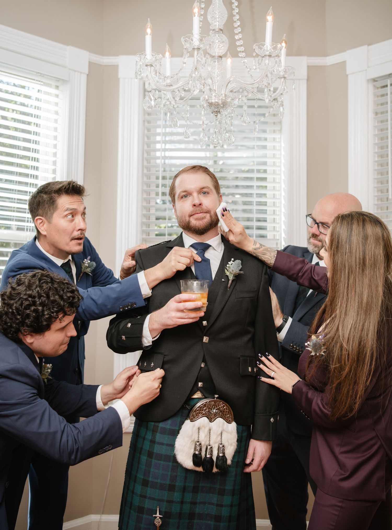 Multiple hands assist with adjusting formal attire under an elegant crystal chandelier.