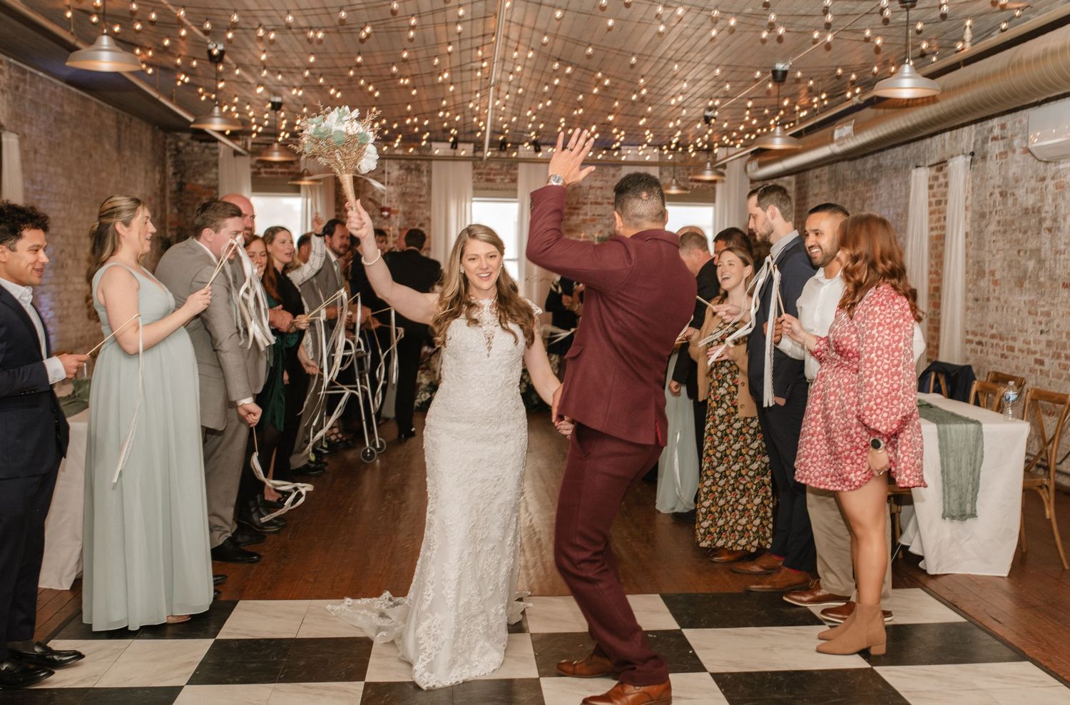 Wedding reception venue with string lights and guests dancing on wooden floor.
