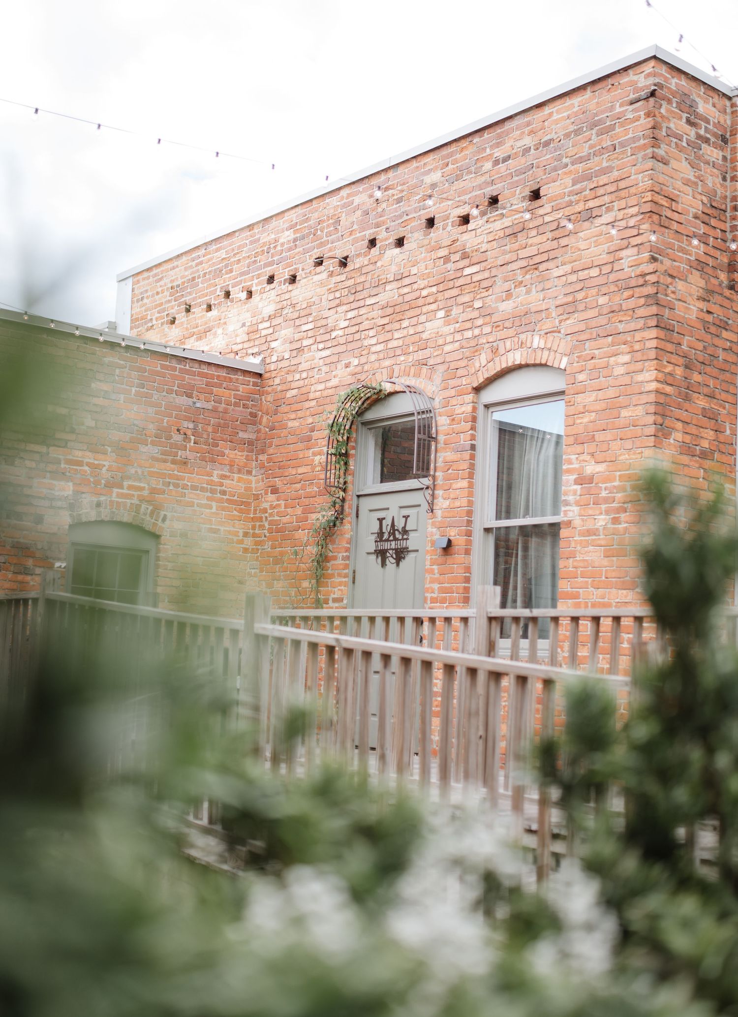 Historic brick building exterior with white-trimmed windows viewed through foliage.