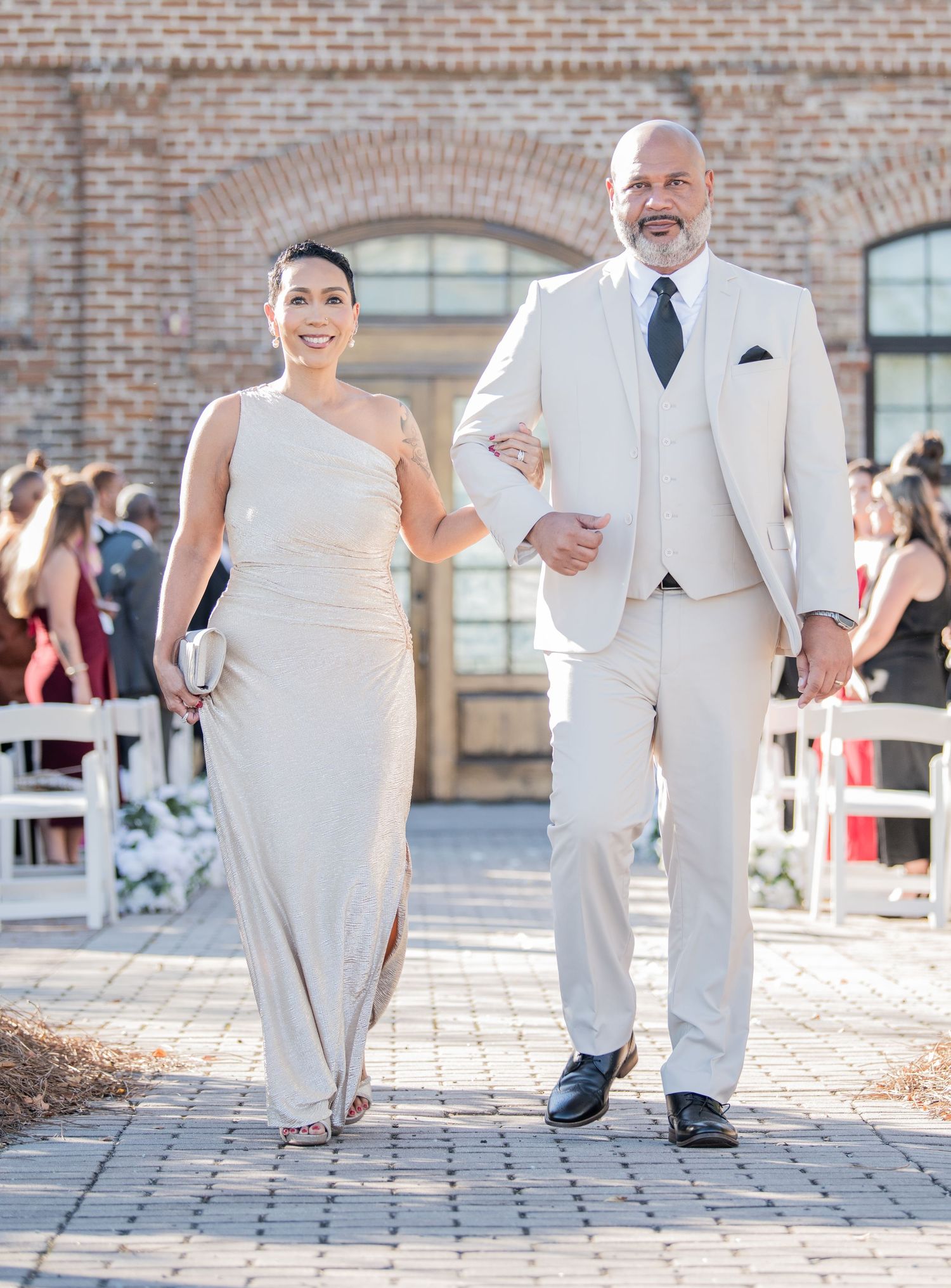 Wedding party members in elegant white attire walking down an outdoor ceremony aisle.