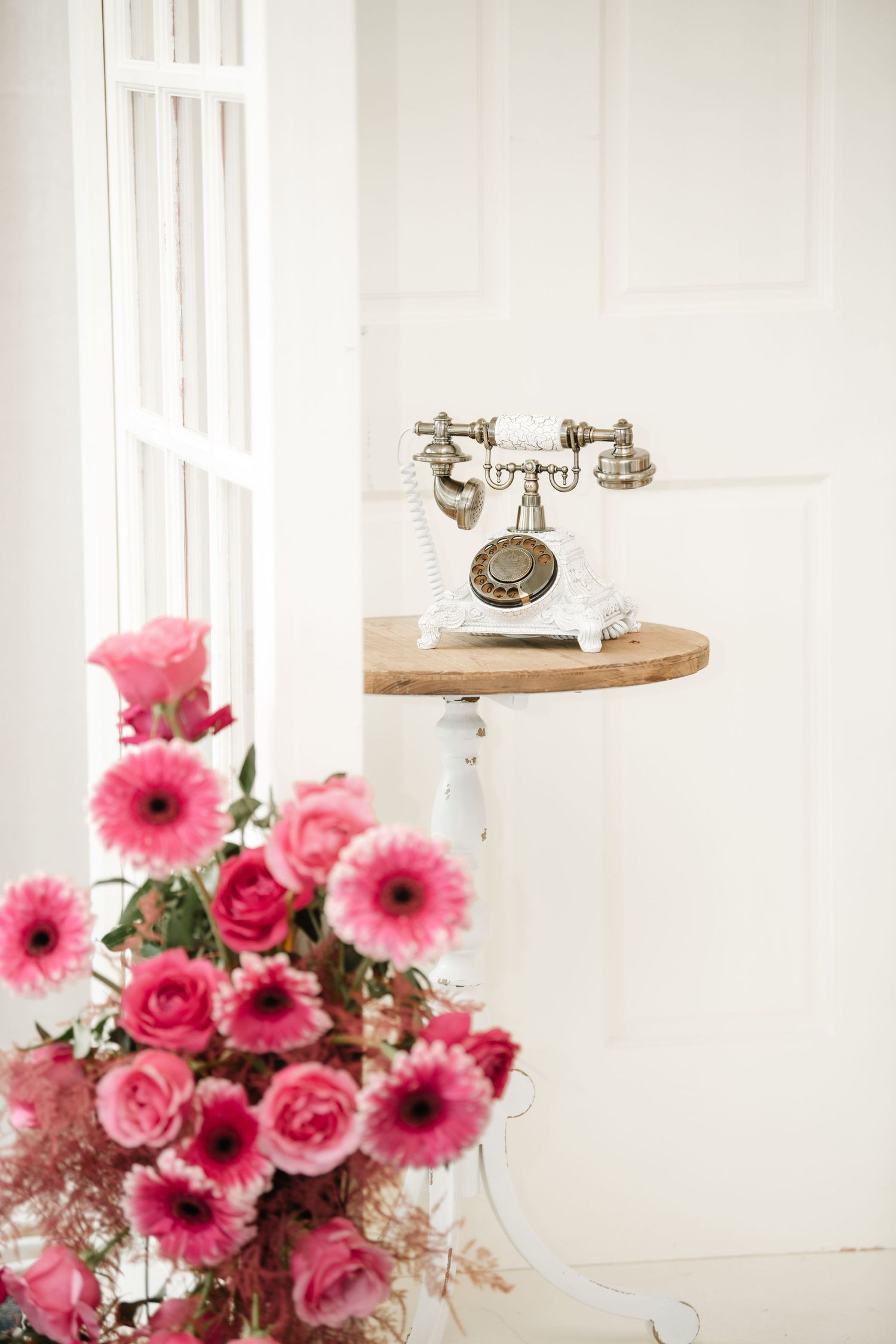 Elegant white interior with vintage telephone and pink gerbera daisy arrangements.