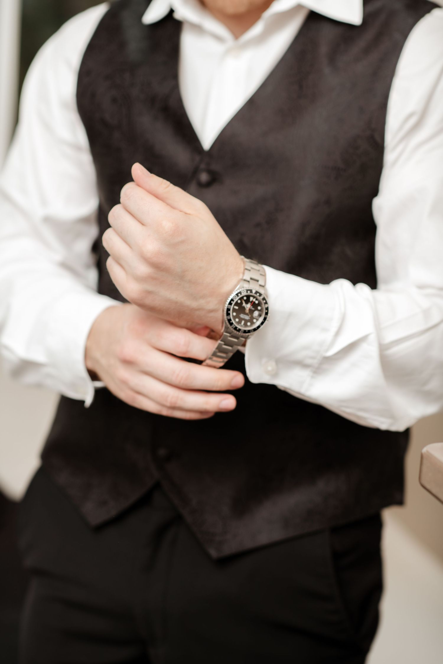 Close-up of formal attire showing black vest and silver watch detail.