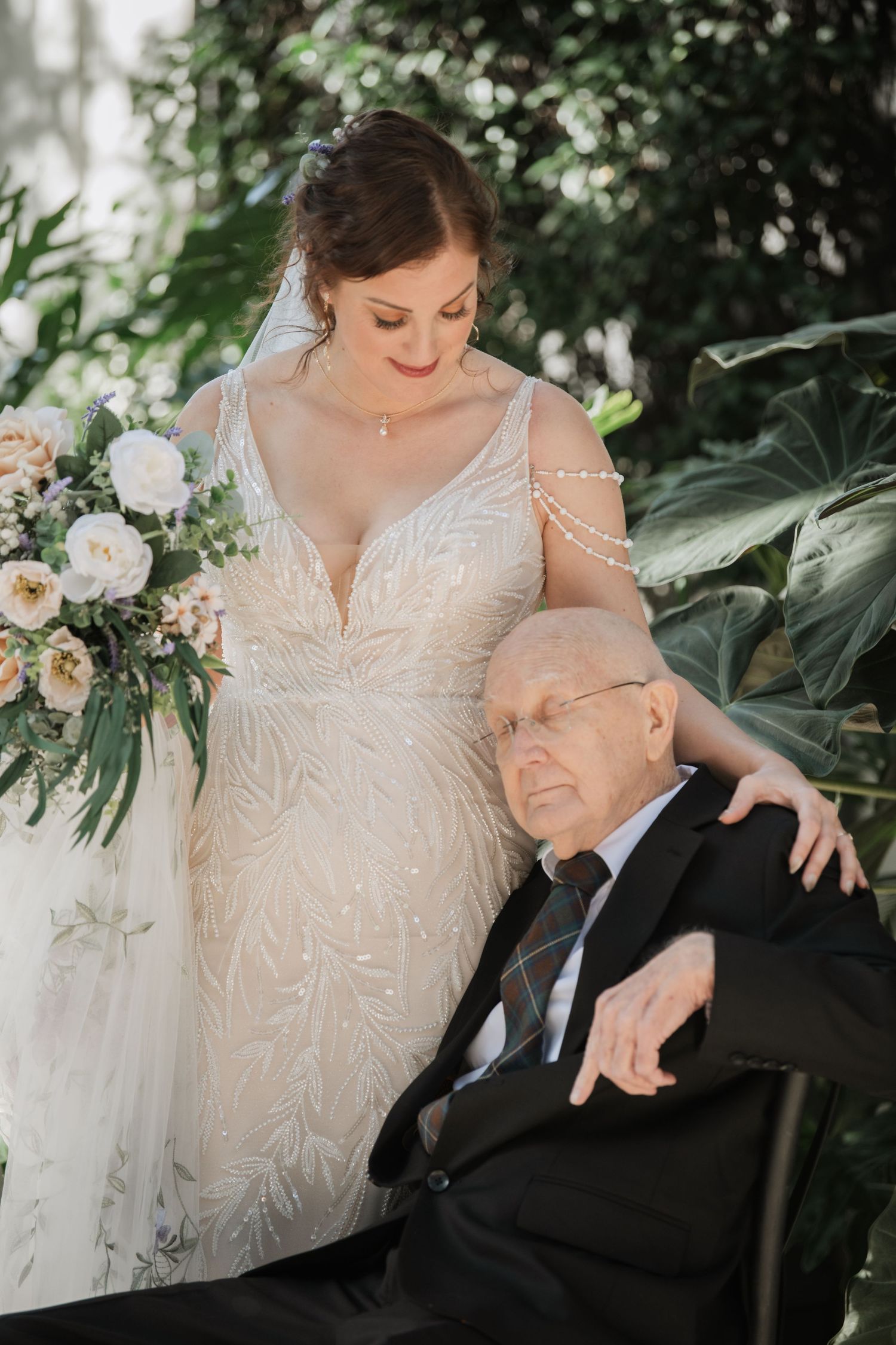 A tender moment captured between a bride in a beaded gown and an elderly guest at a wedding celebration.
