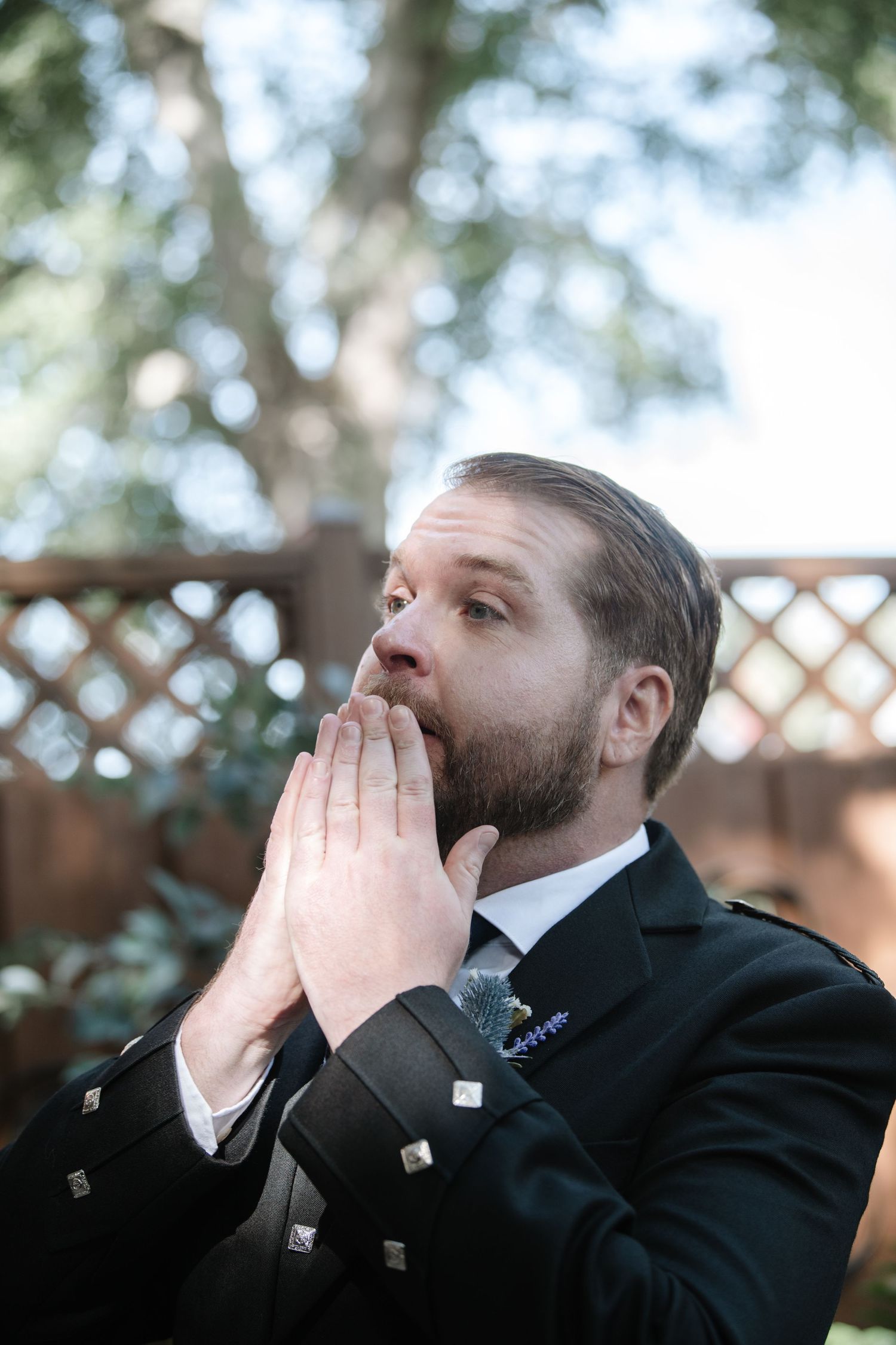 A person in formal Scottish attire shows an emotional moment outdoors.