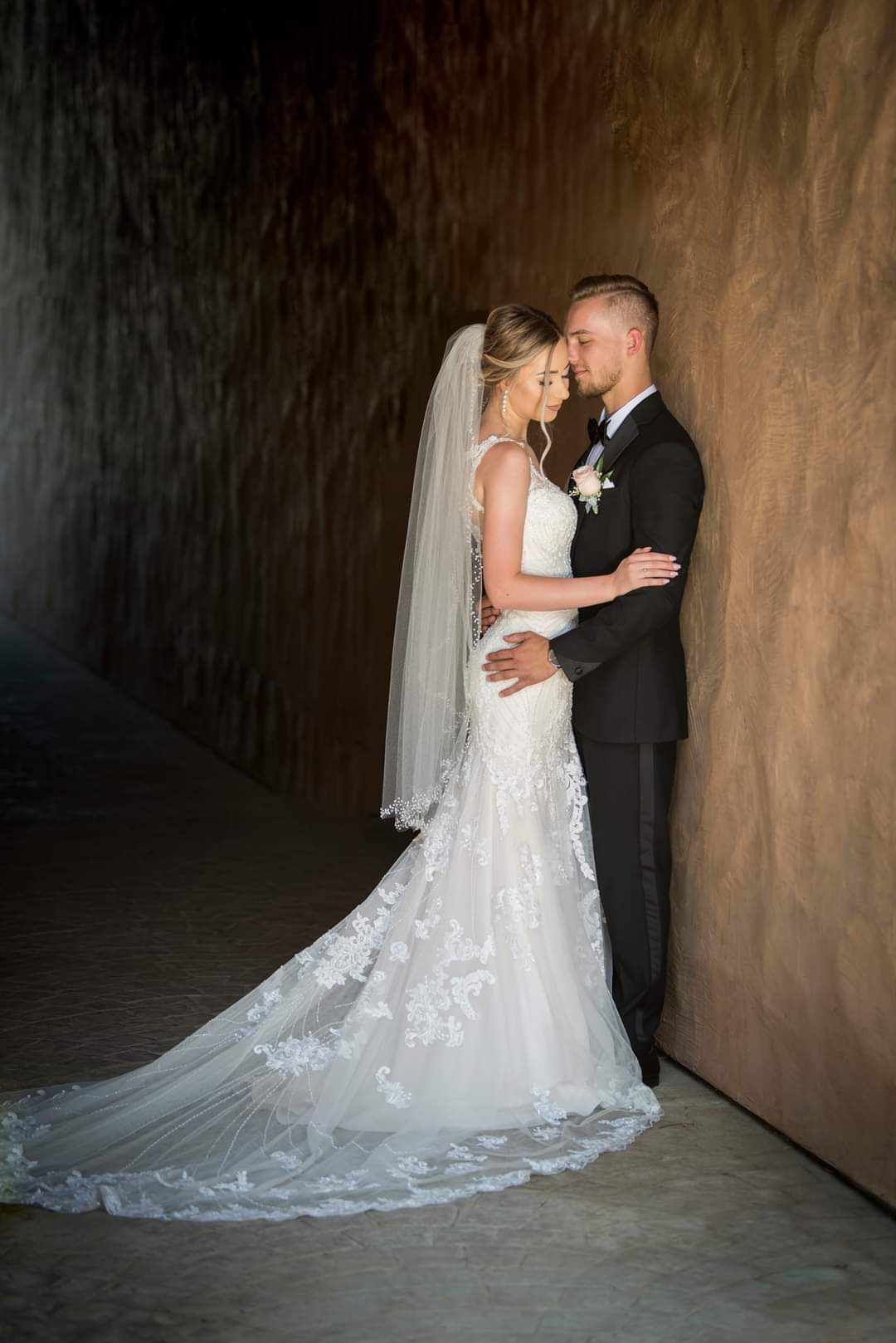 Romantic wedding portraits against a textured wall showcasing a flowing lace train.