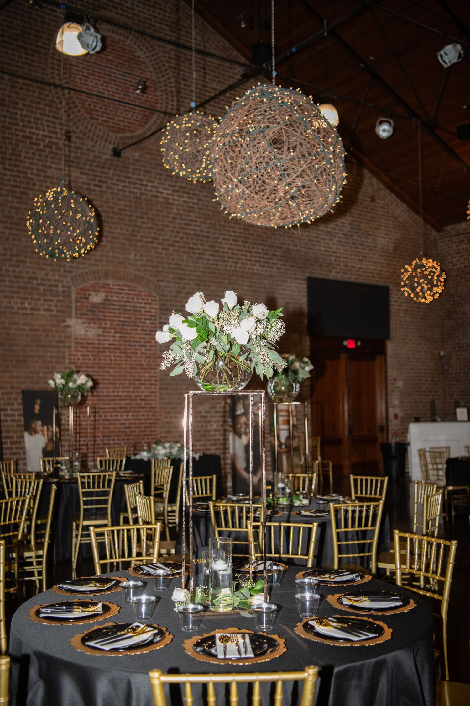 Elegant wedding reception setup with crystal chandeliers and gold chiavari chairs in a brick venue.