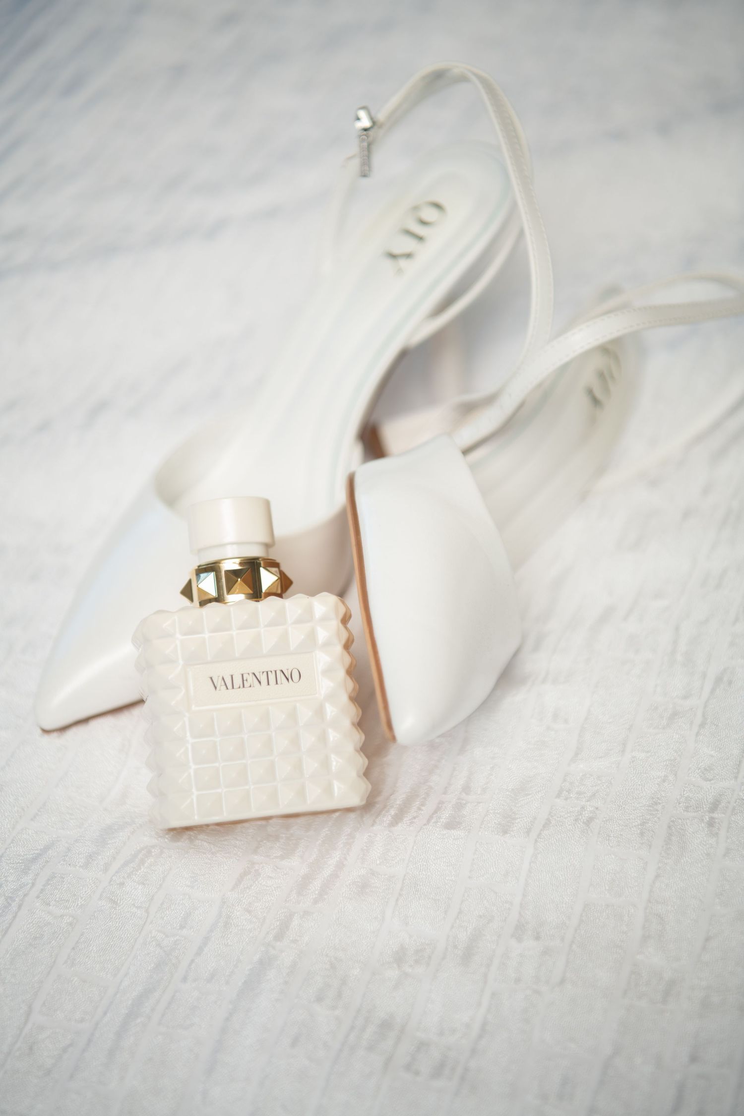 White designer wedding shoes with quilted pattern displayed on textured surface.