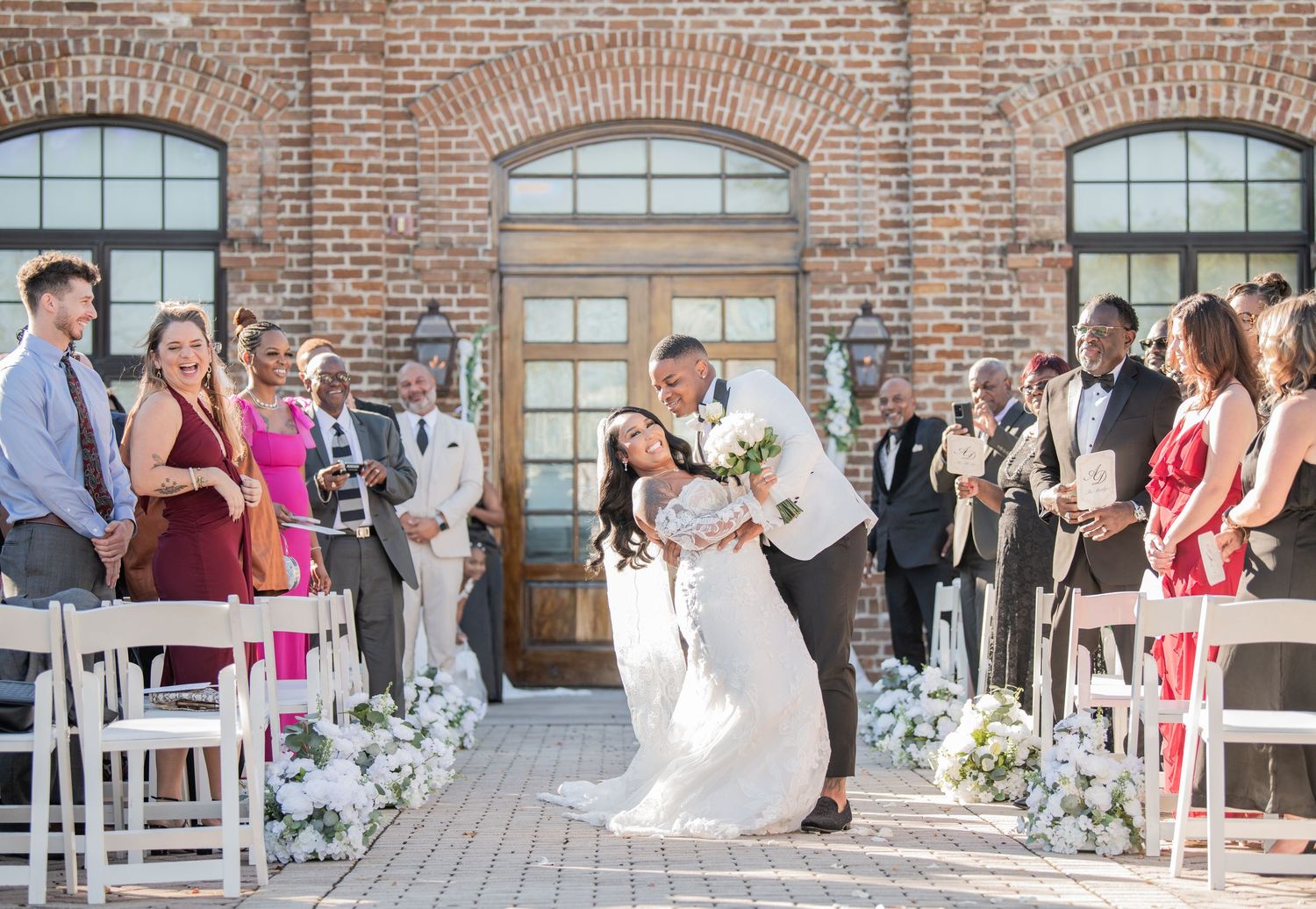 Wedding ceremony moment at a historic brick venue with guests watching from white chairs.