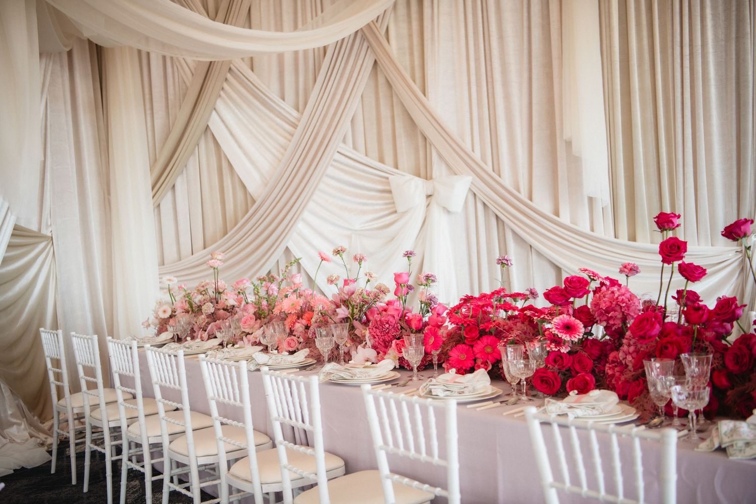 Romantic wedding venue setup with white draping and pink floral accents.
