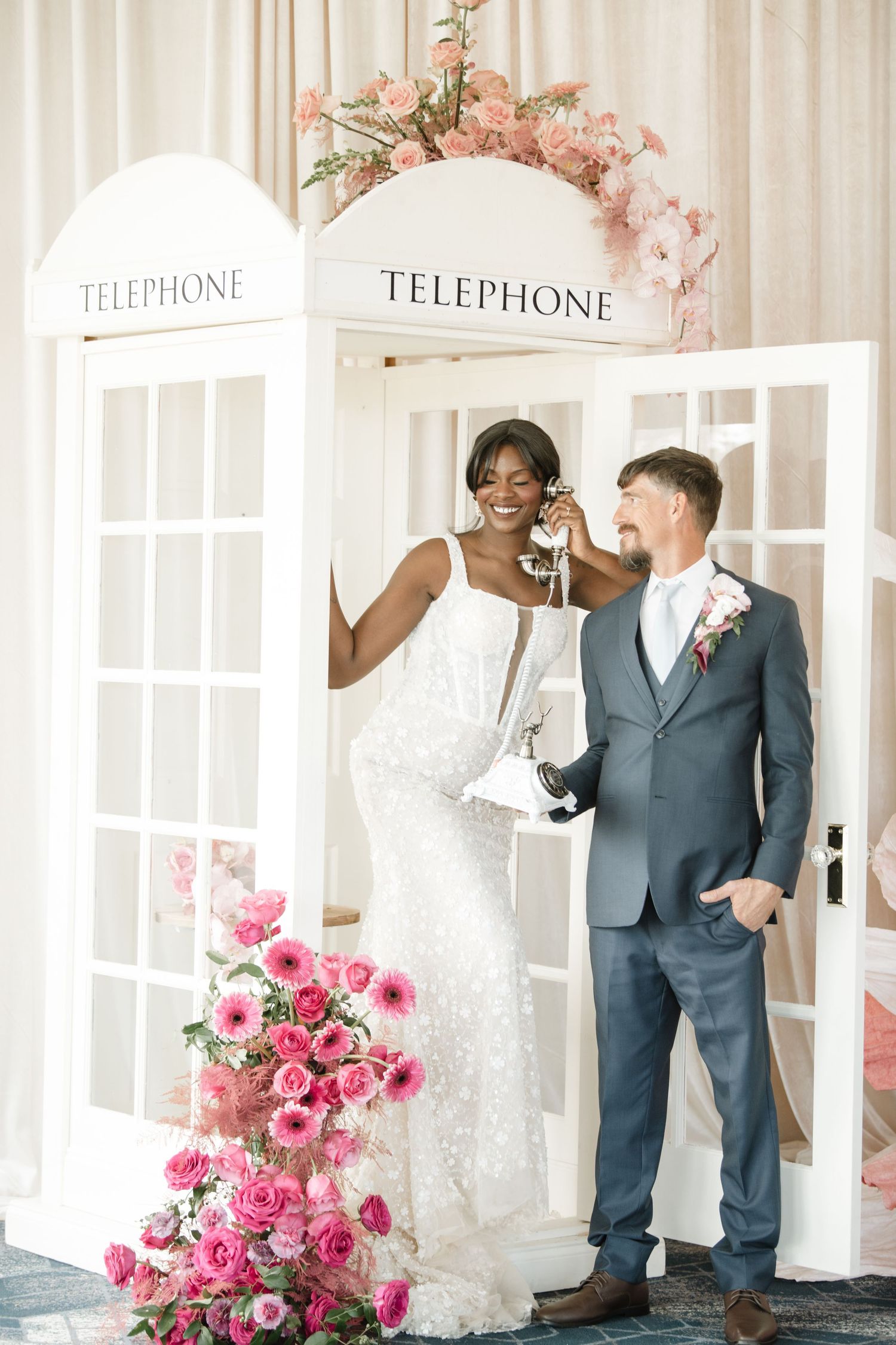 Playful wedding portraits with vintage telephone booth and pink roses as decor.