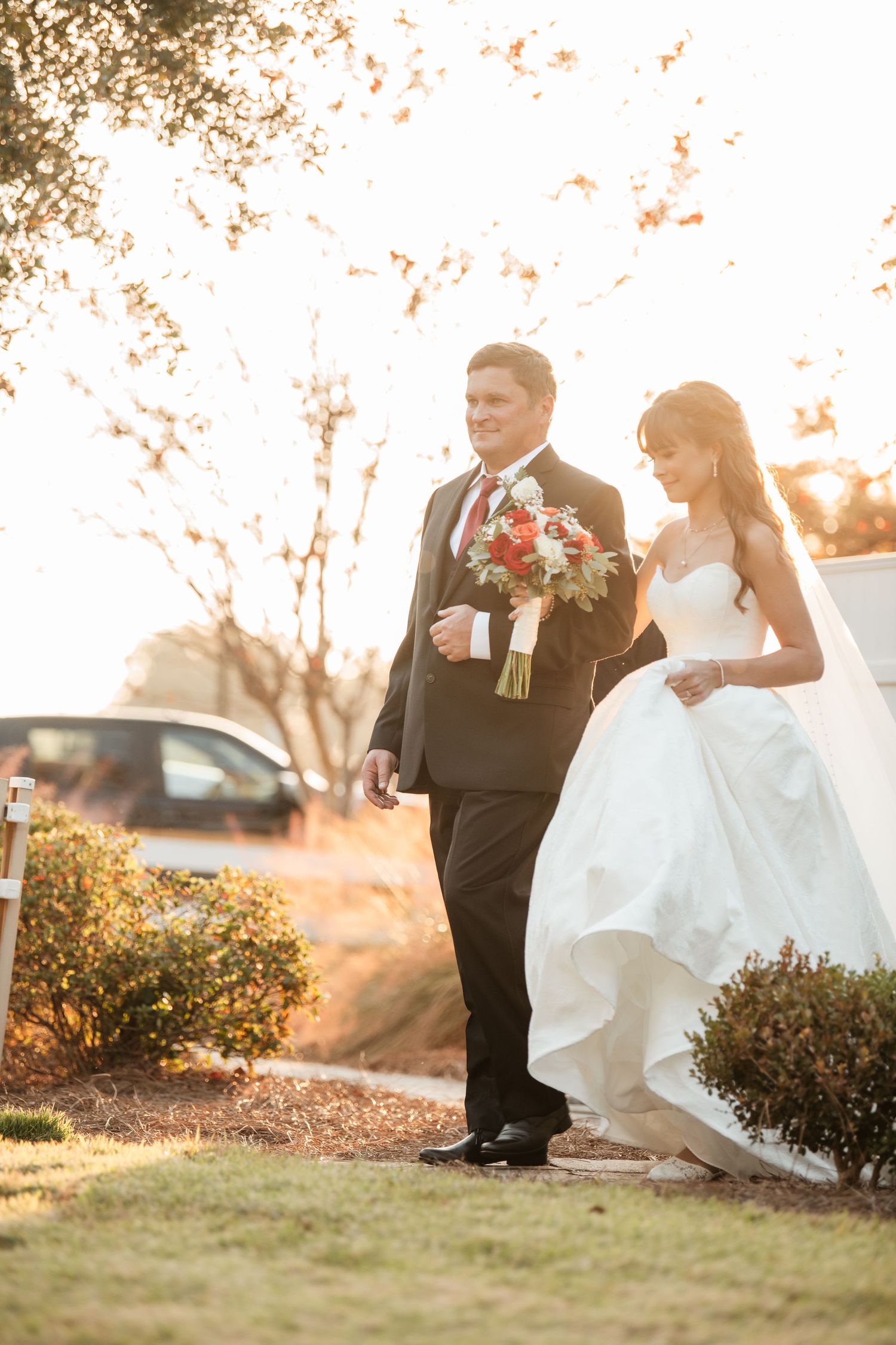 Wedding couple and attendants walk together on garden path at sunset.