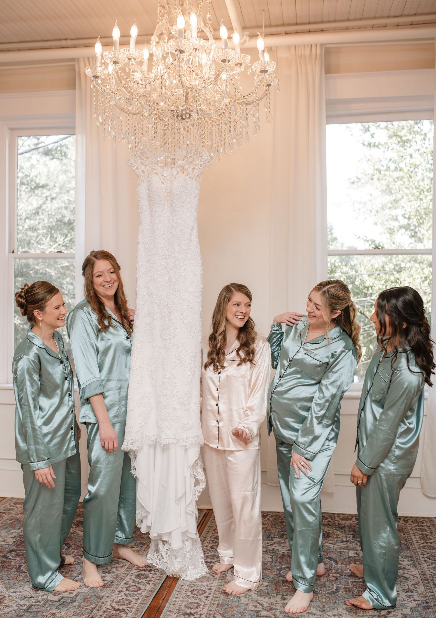 Wedding party wearing matching silk pajamas posing under crystal chandelier.
