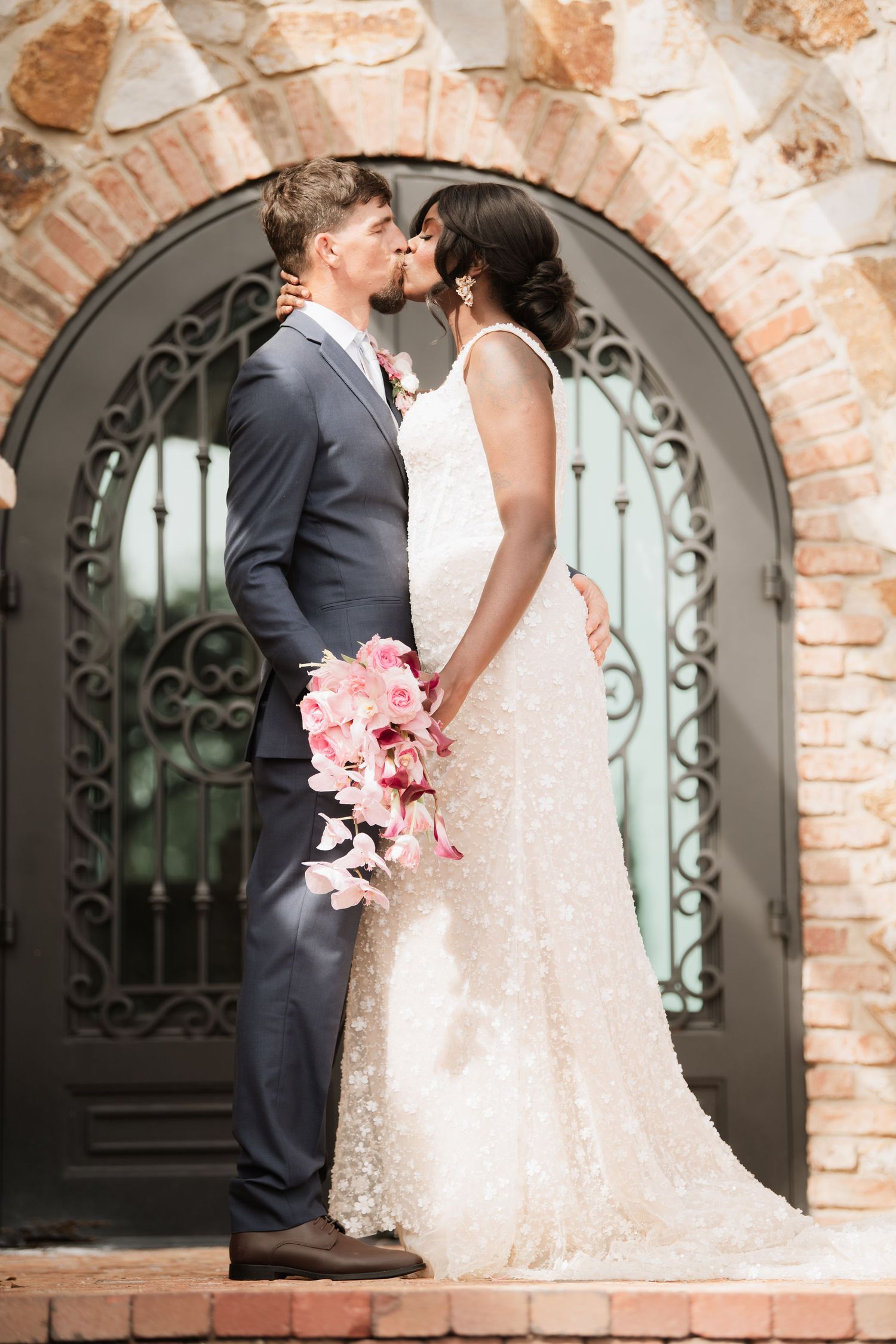 Newlyweds share a tender moment against a backdrop of exposed brick and an elegant arched doorway.