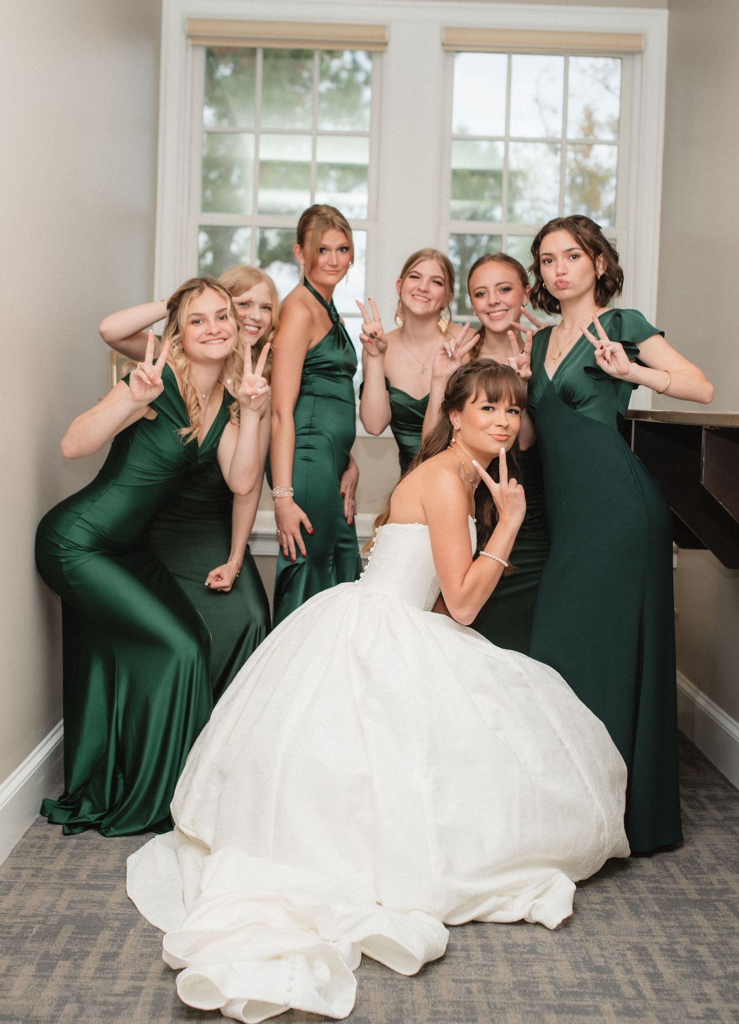 Playful wedding party photos with bridesmaids in emerald green dresses posing with the bride.