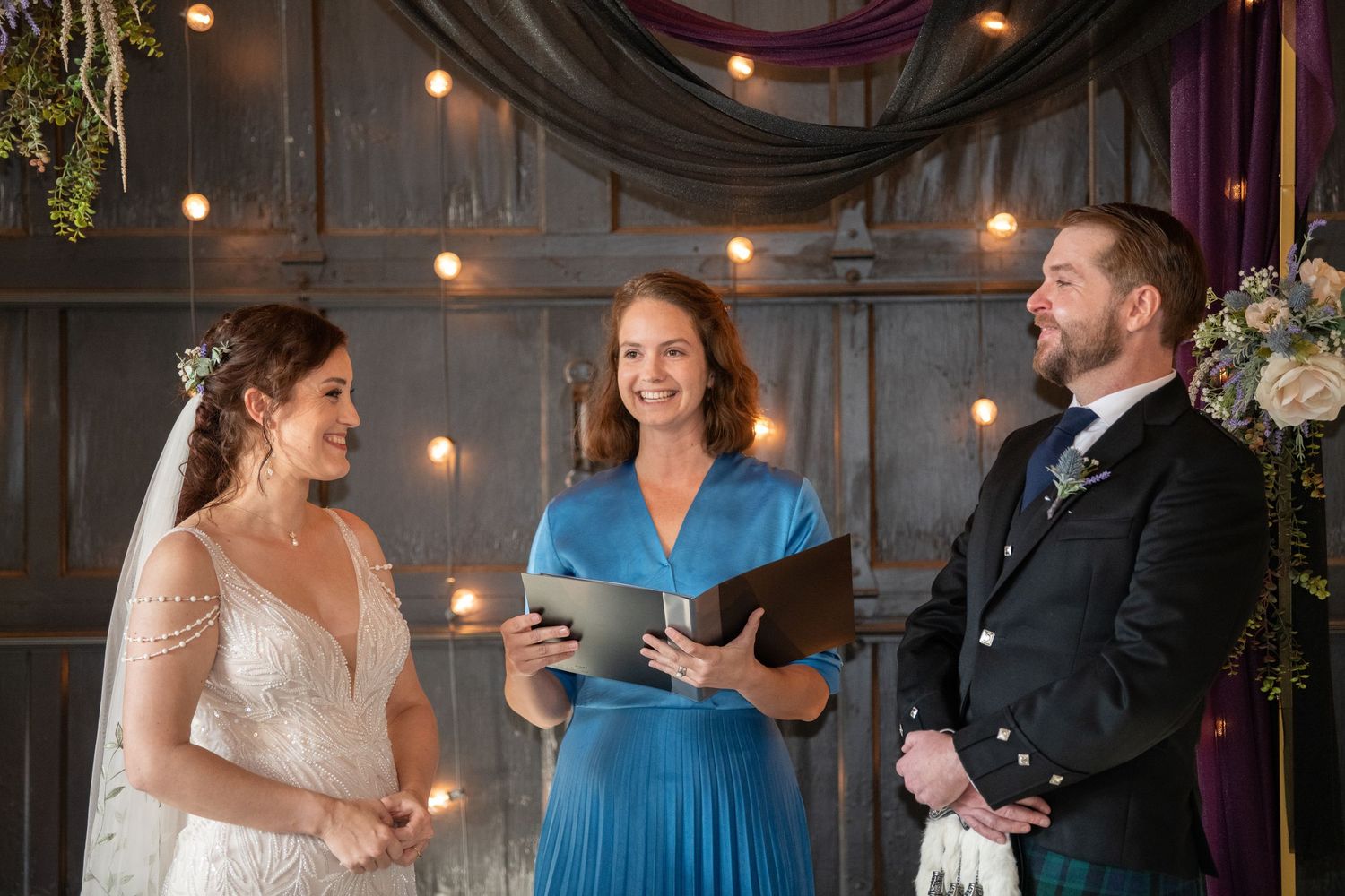 Wedding ceremony with officiant in blue dress and groom in traditional Scottish kilt.