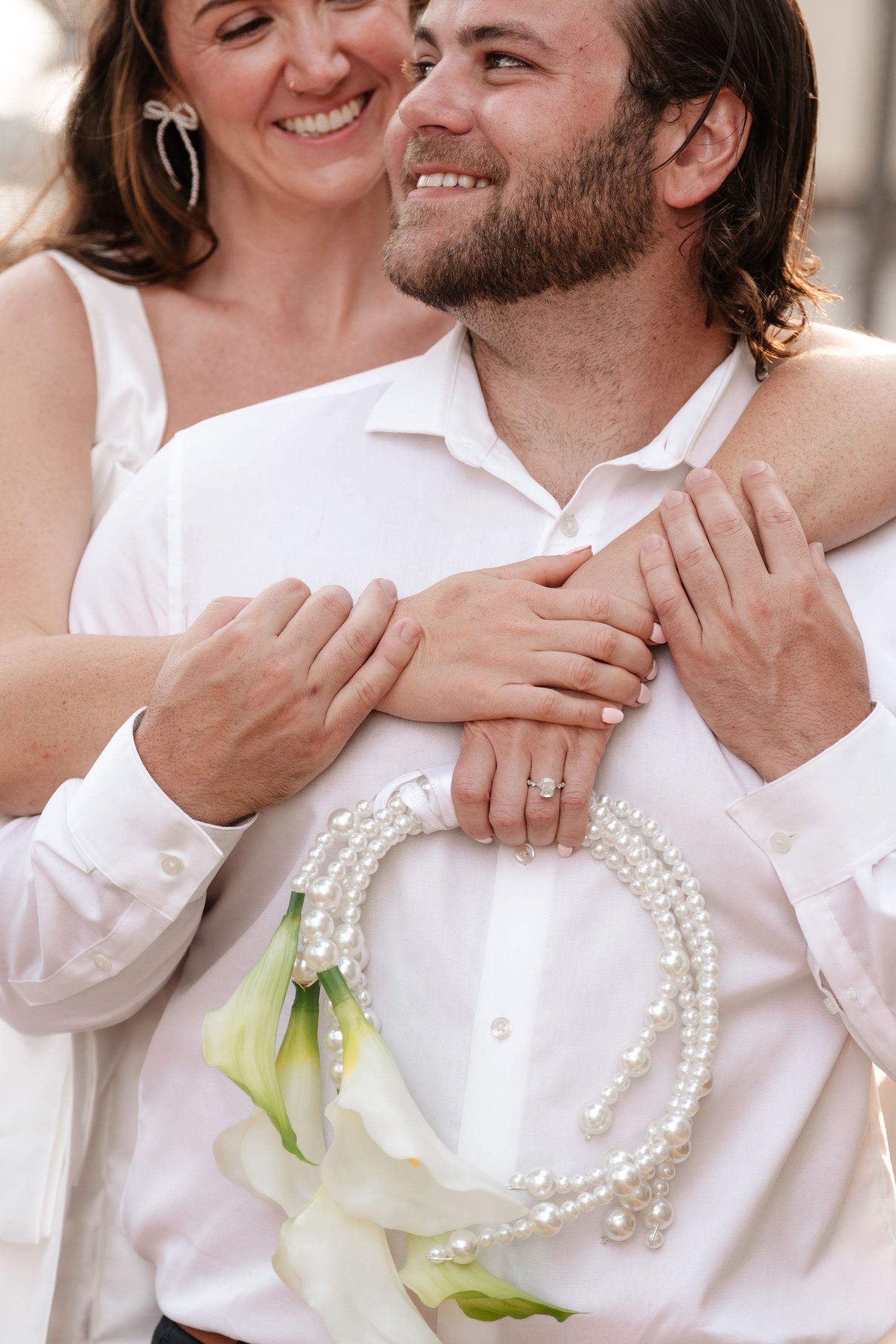 Close-up shots of couple wearing white with pearl necklace and floral boutonniere.