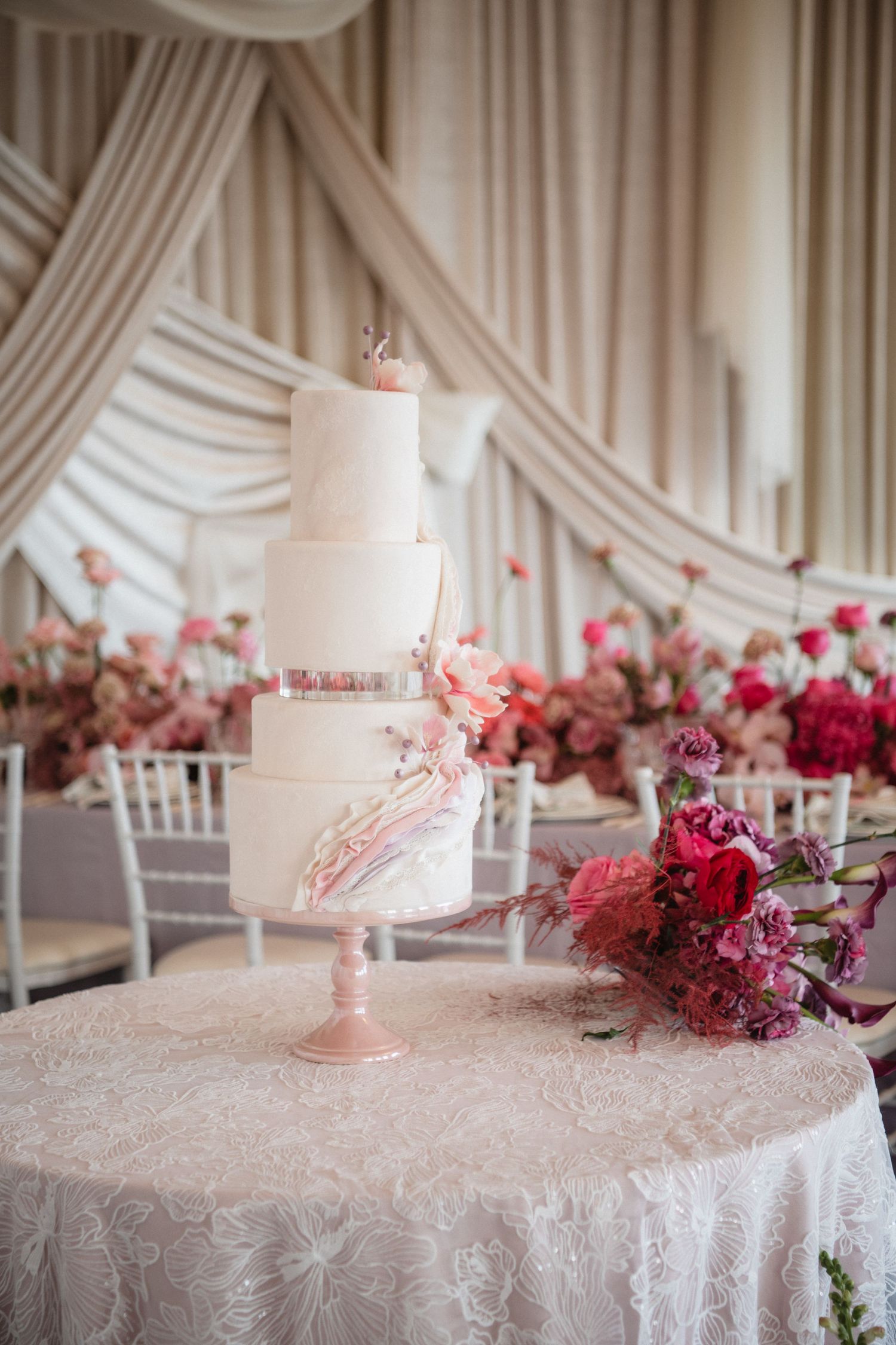 Elegant wedding table setting with pink floral arrangements and draped white fabric backdrop.