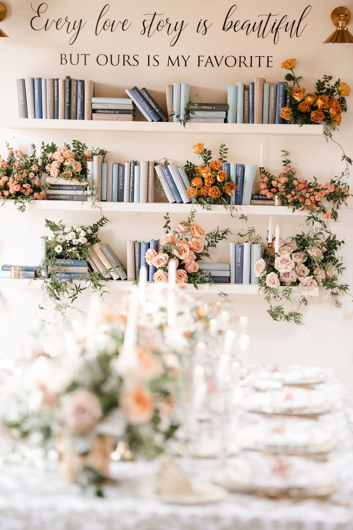 Elegant white bookshelves decorated with peach and orange floral arrangements and greenery for a romantic wedding setting.