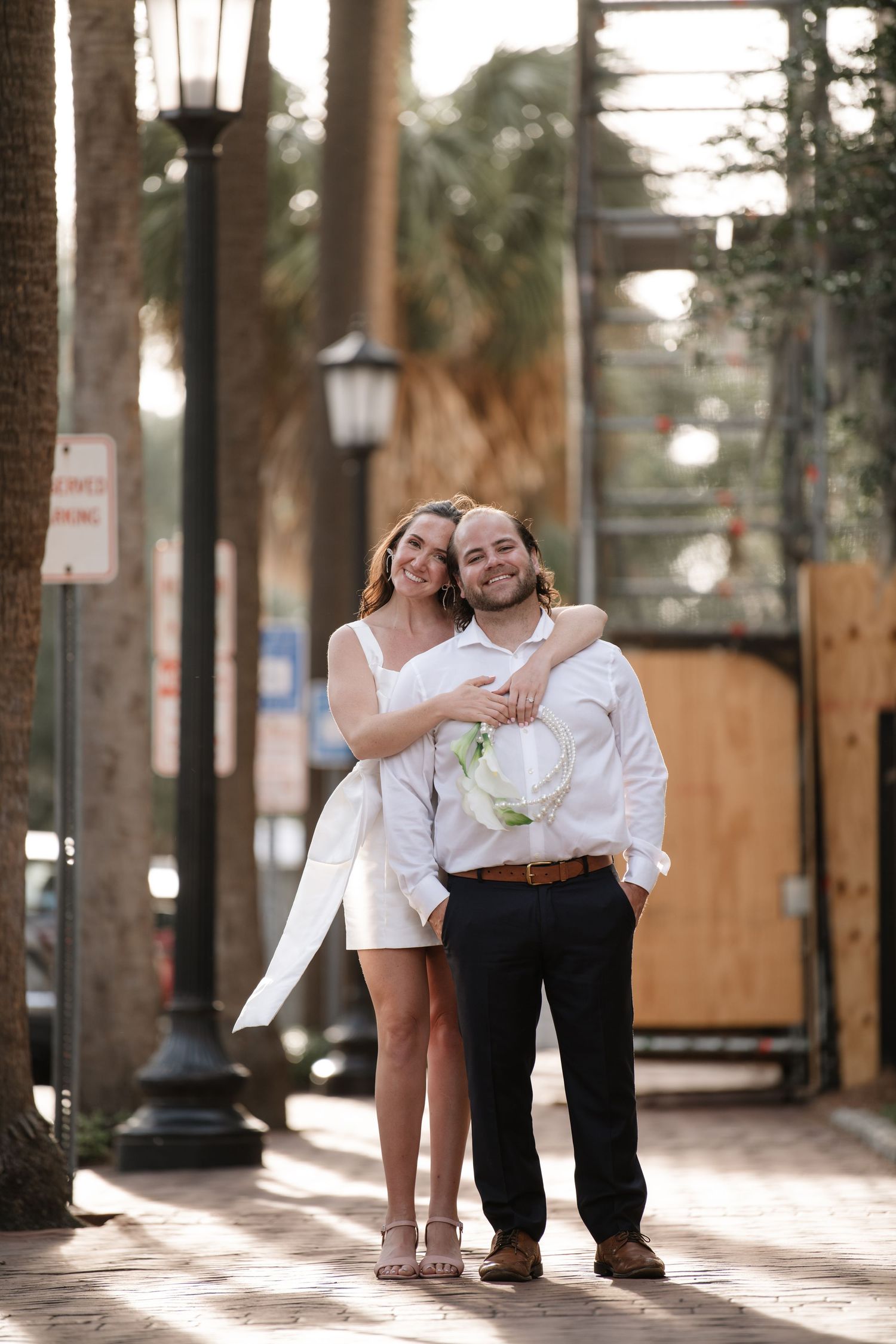 A romantic engagement photo series showing a couple in white and black outfits embracing in an outdoor urban setting.