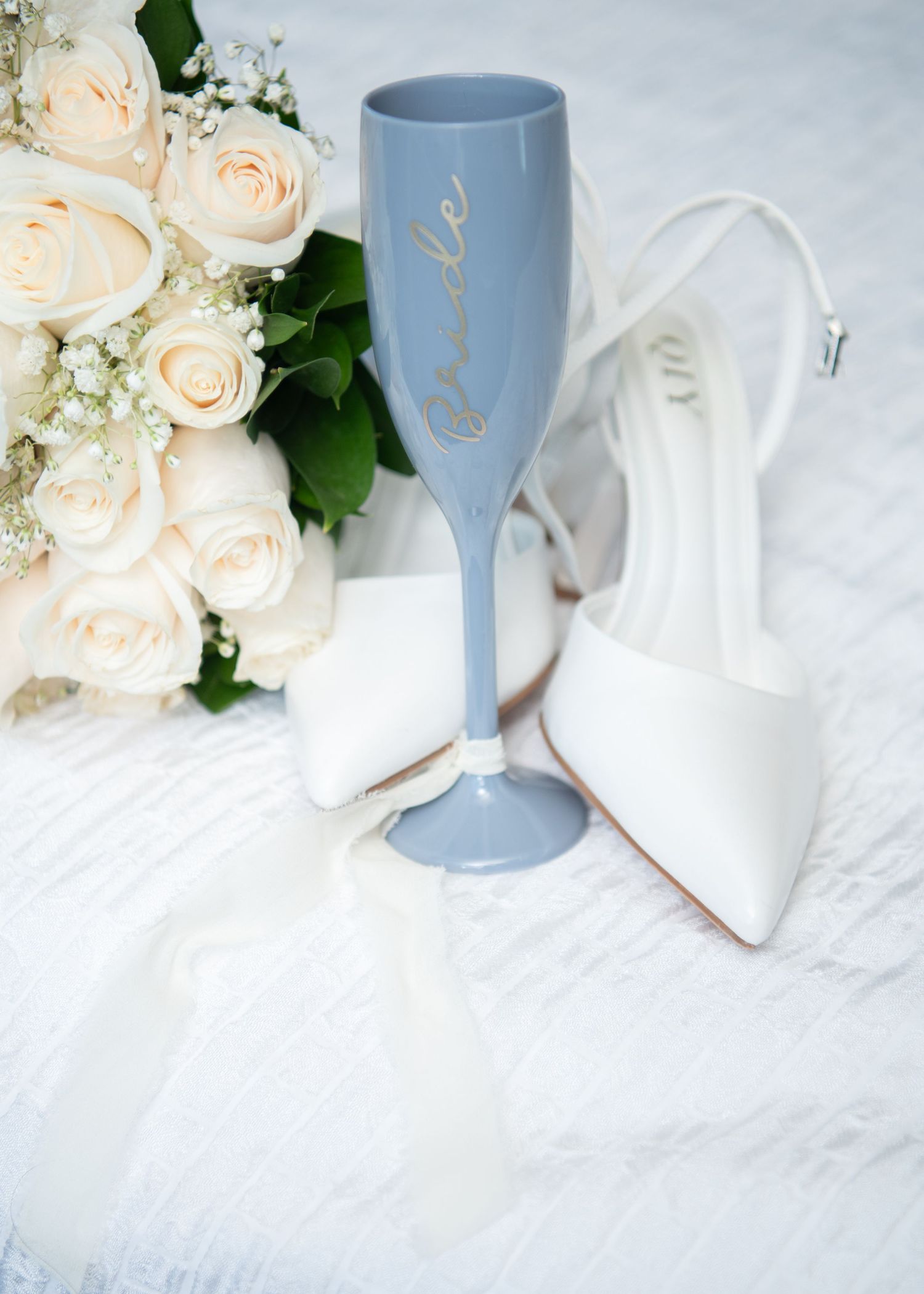 Elegant wedding table setting with white roses and pale blue goblet on white tablecloth.