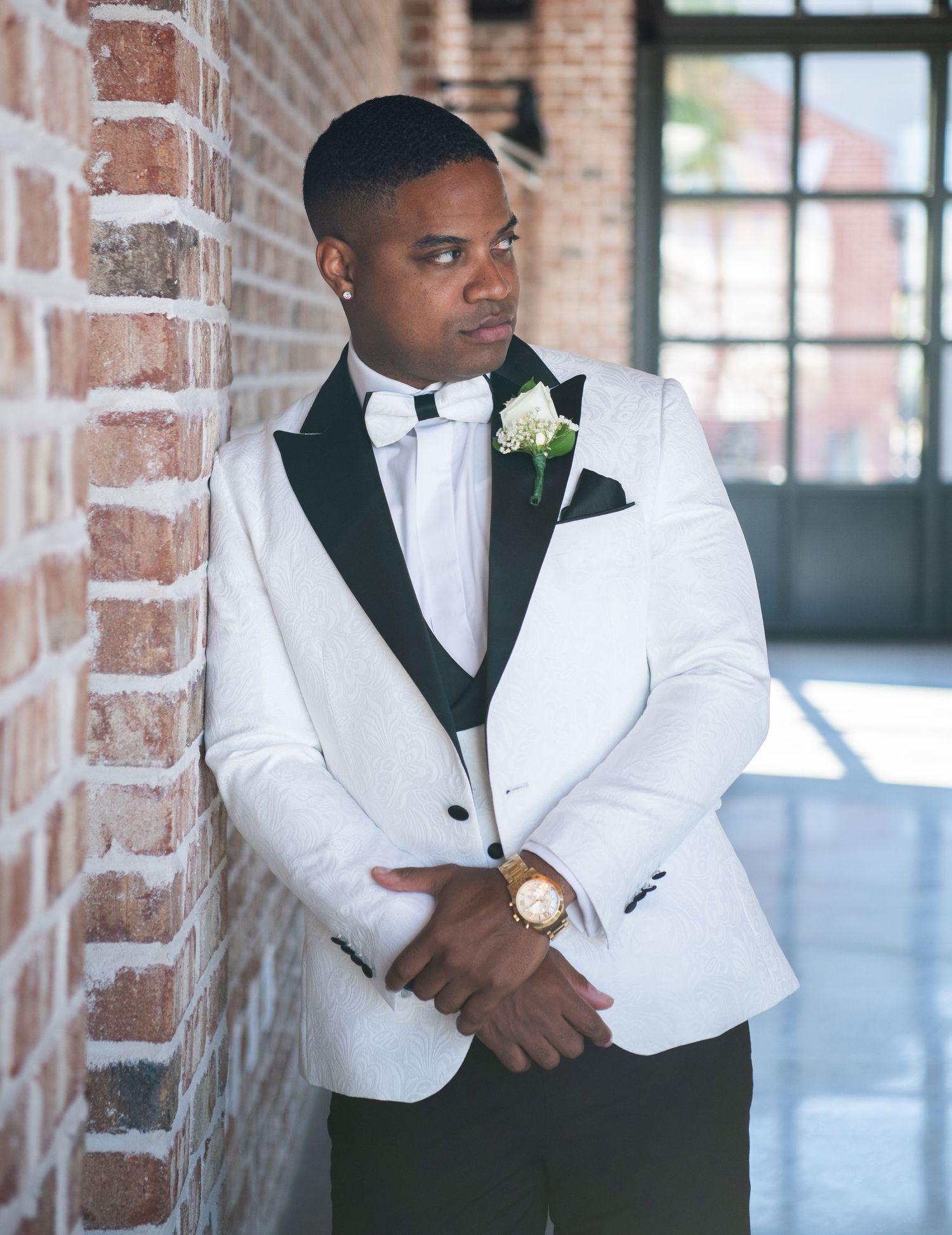 Formal portraits of groomsman in white dinner jacket against brick wall backdrop.