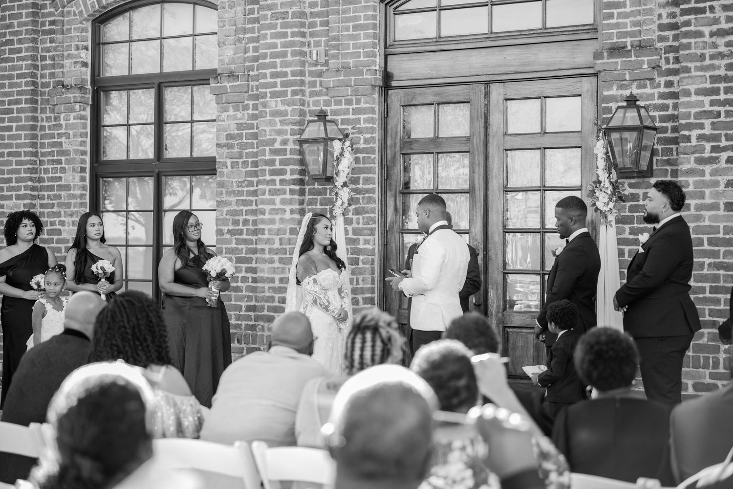 Guests stand in formal attire against a historic brick building exterior.
