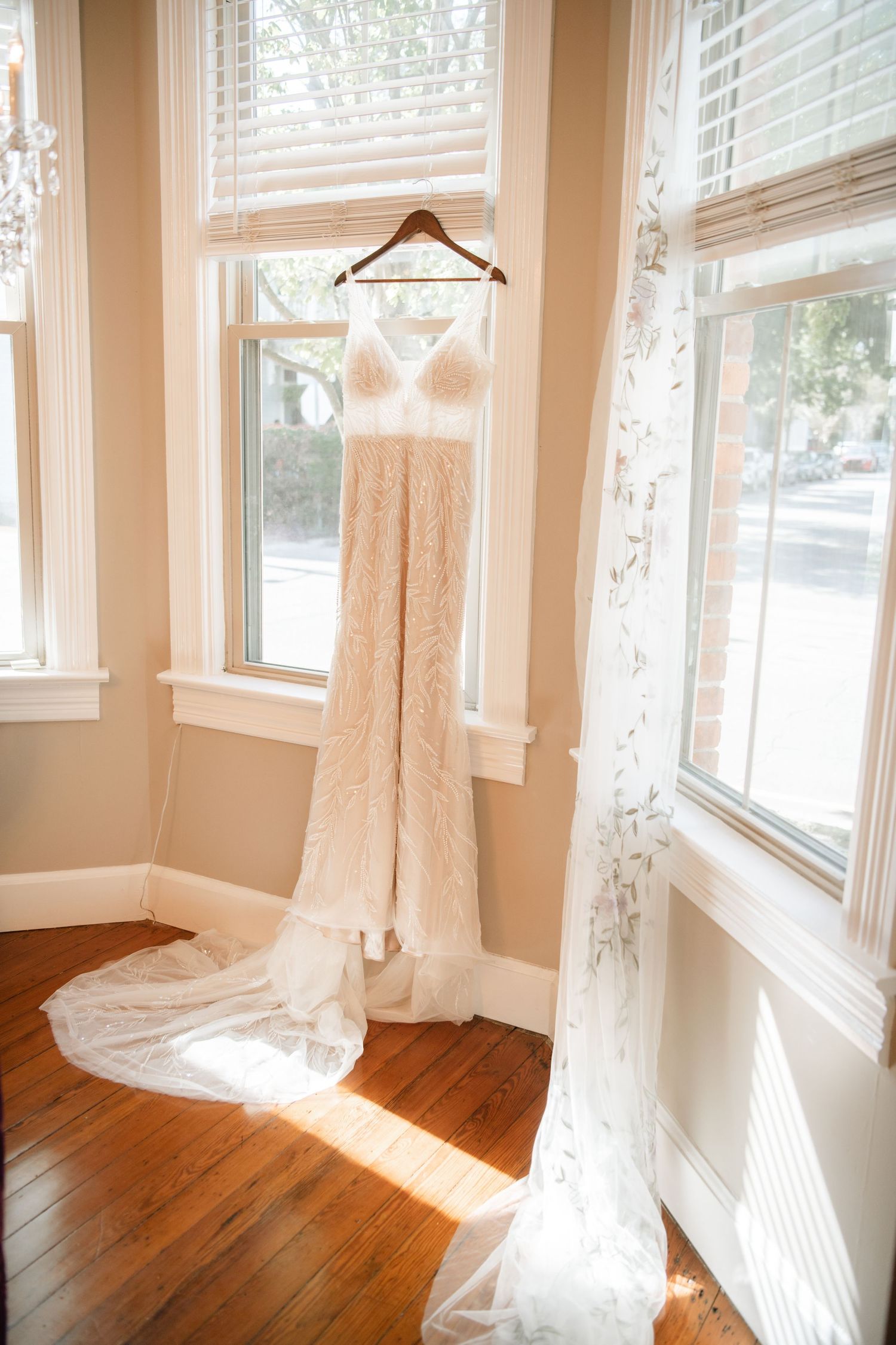 Sunlit room with hardwood floors and multiple windows draped with sheer white curtains.