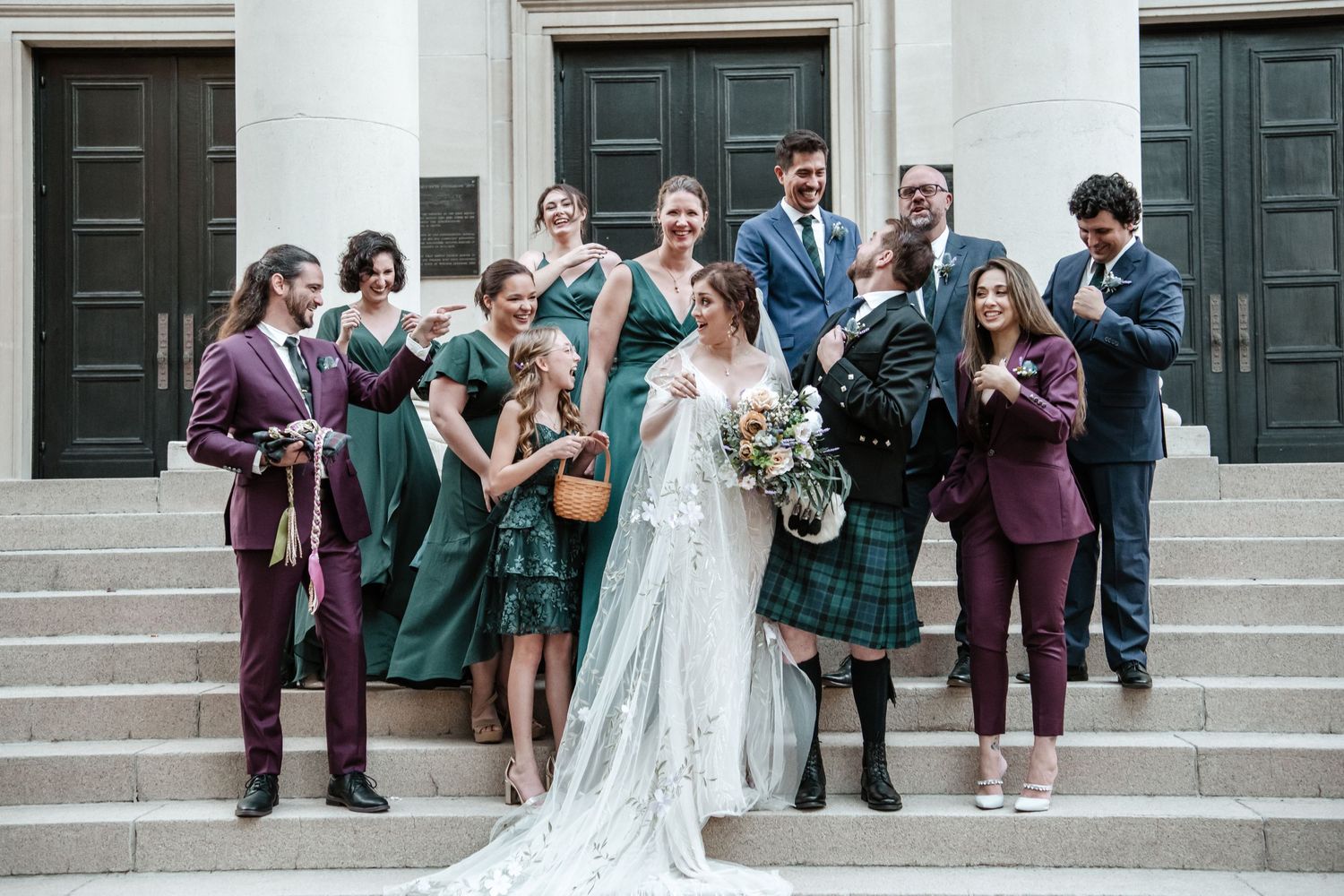Wedding party and guests watching and cheering from stone steps of a white building.