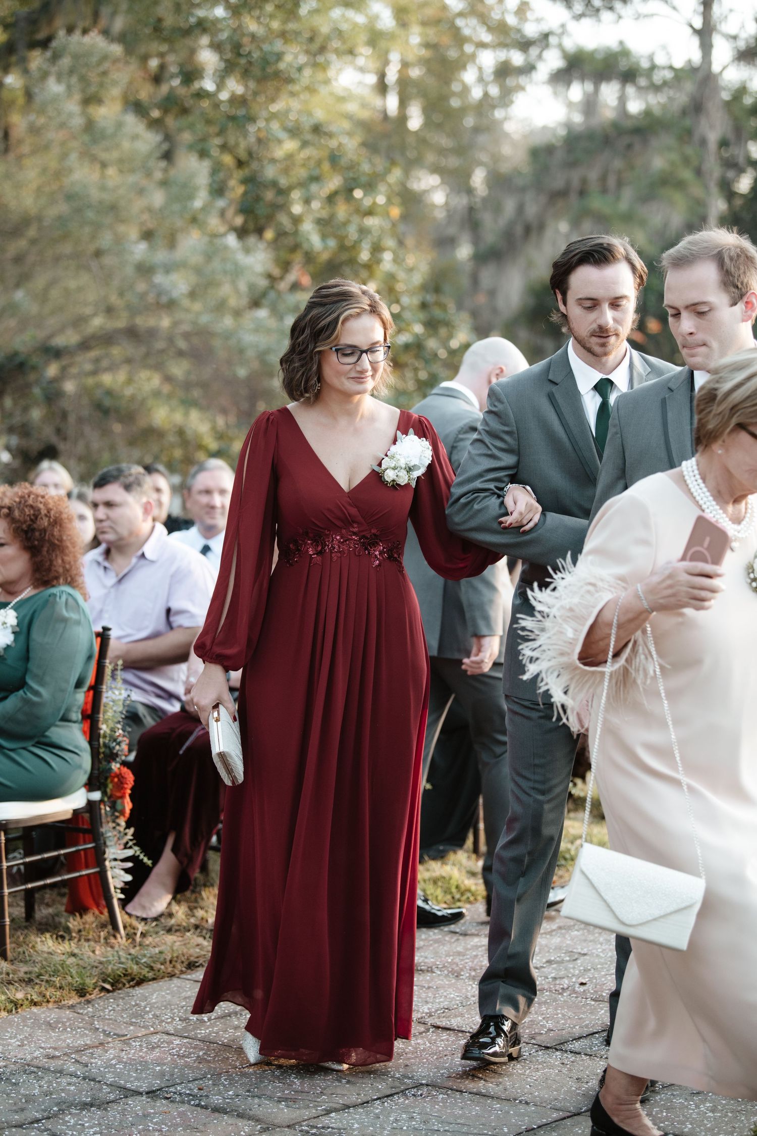 Wedding attendees in burgundy and formal attire interact during an outdoor celebration.