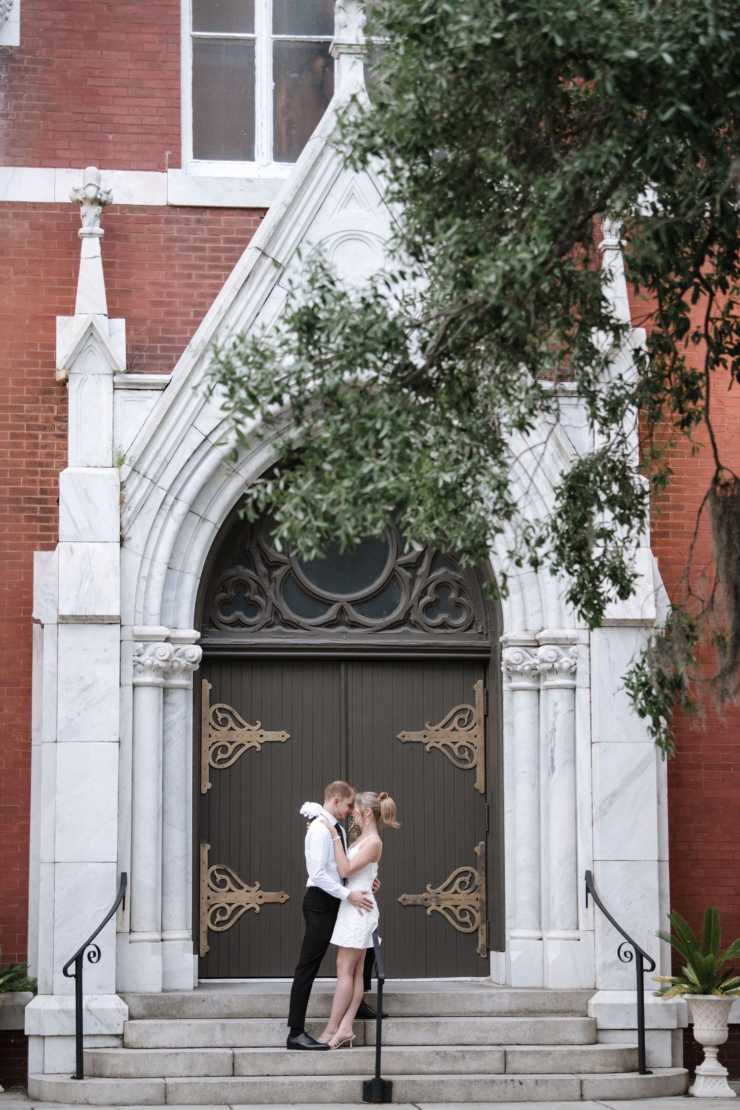 A romantic embrace captured in front of a grand church entrance with gothic architectural details.