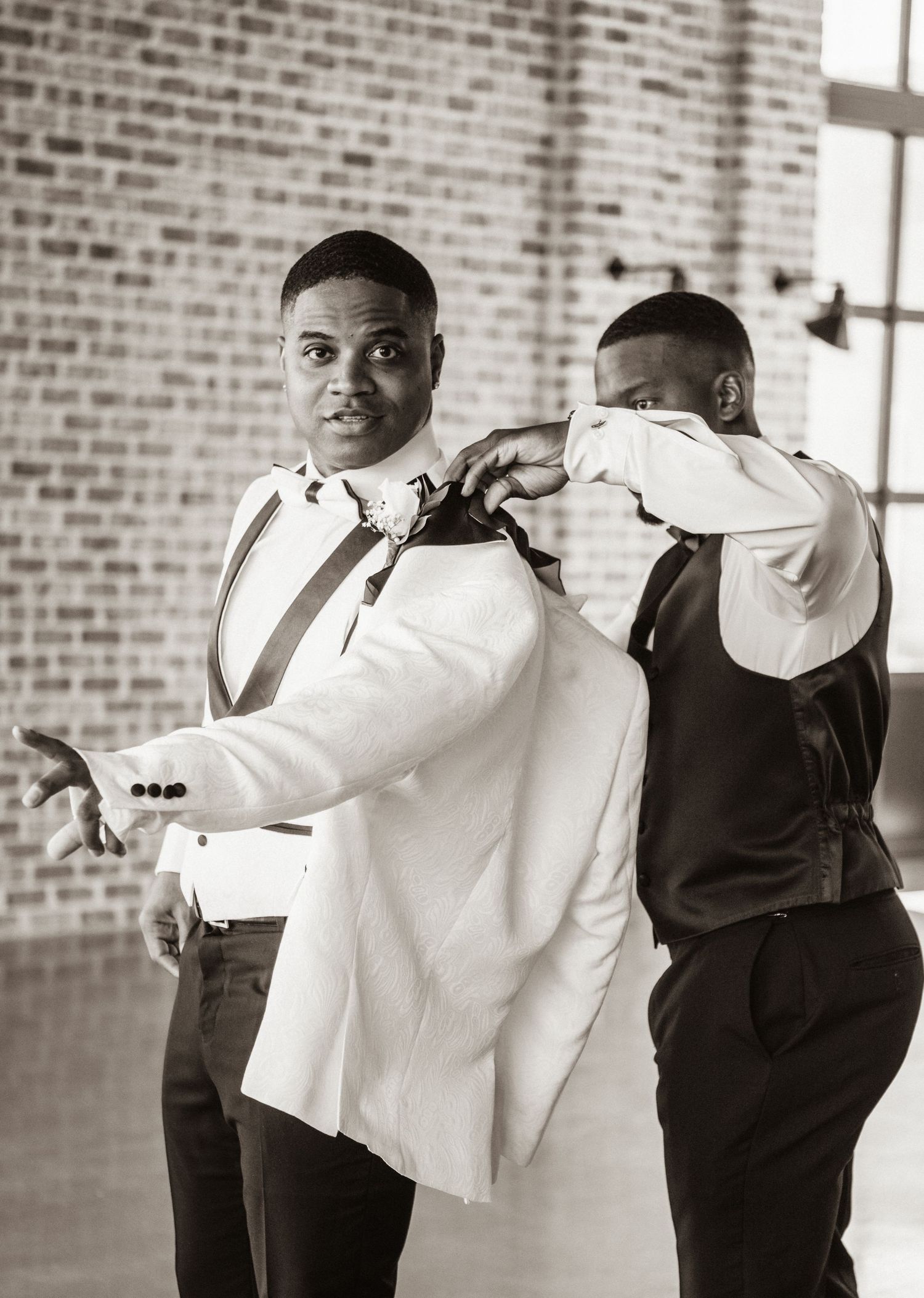 Groomsmen help each other put on white tuxedo jackets before wedding ceremony.
