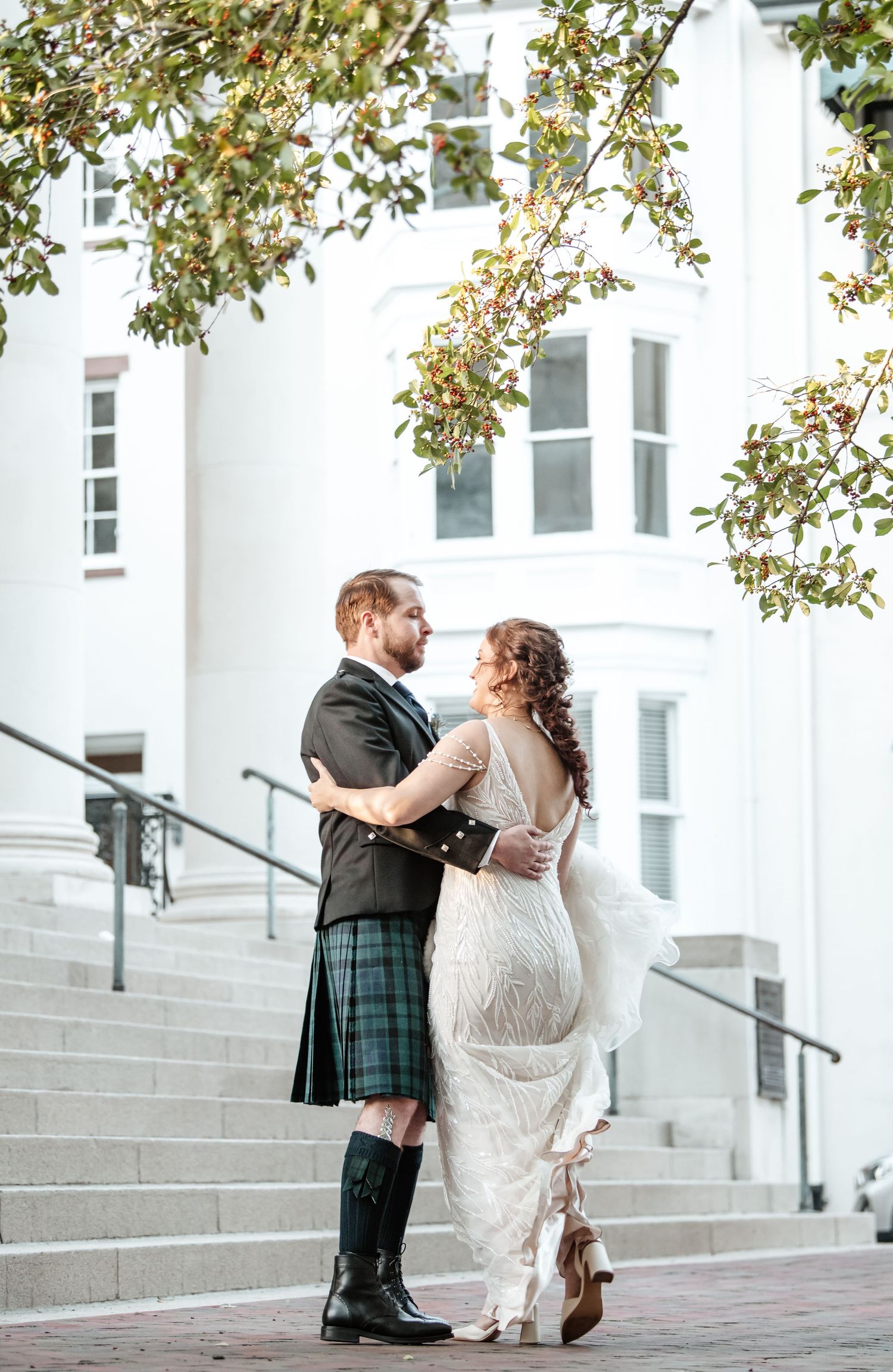 A romantic wedding couple dancing together on stone steps in front of a white building.