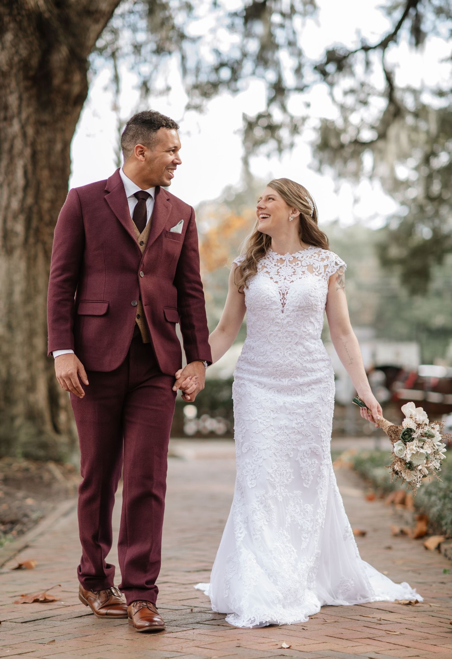 Wedding couple poses for romantic outdoor portraits on brick pathway surrounded by trees.