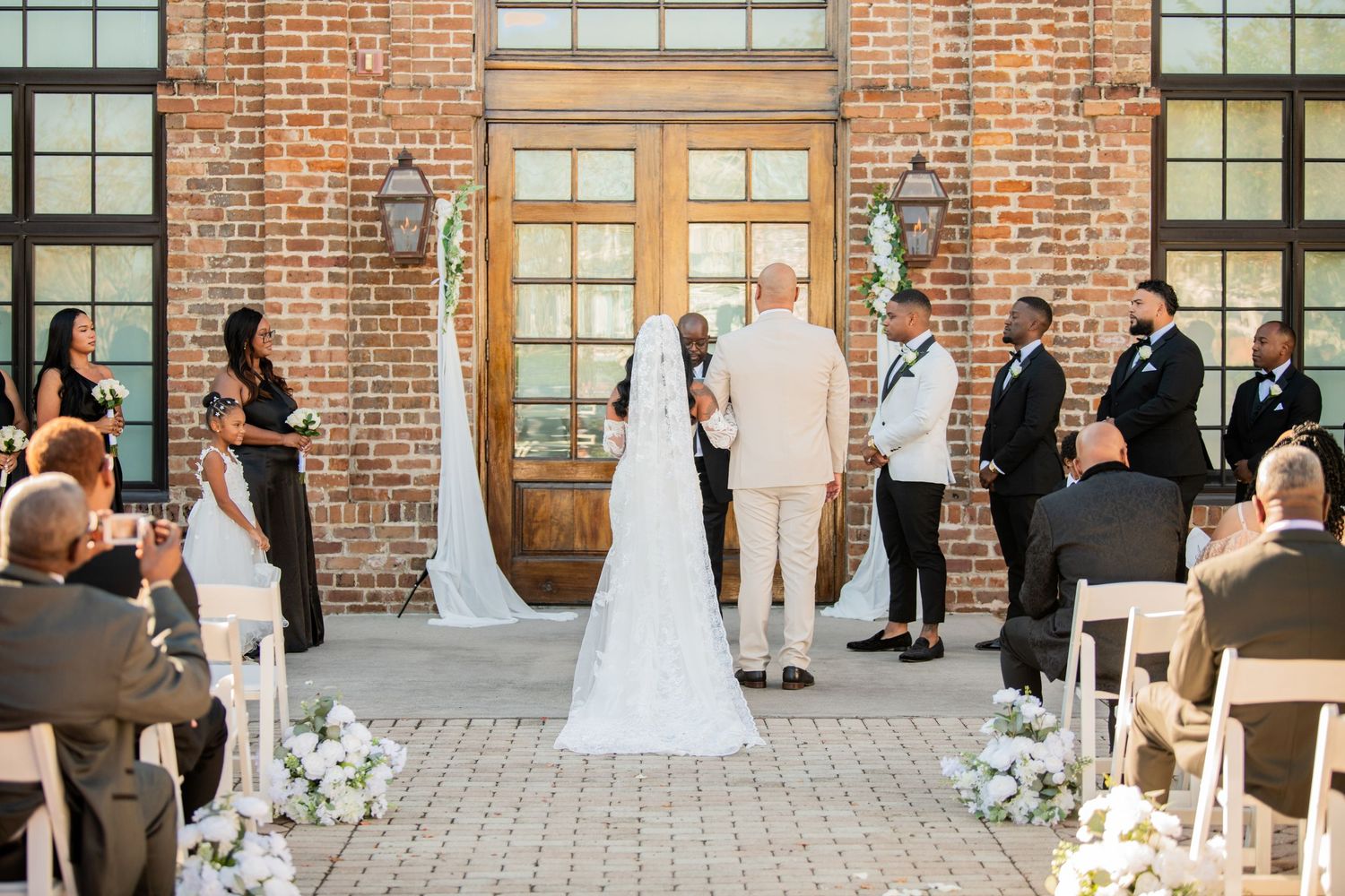 Wedding ceremony setup with white chairs against industrial brick backdrop and floral decorations.