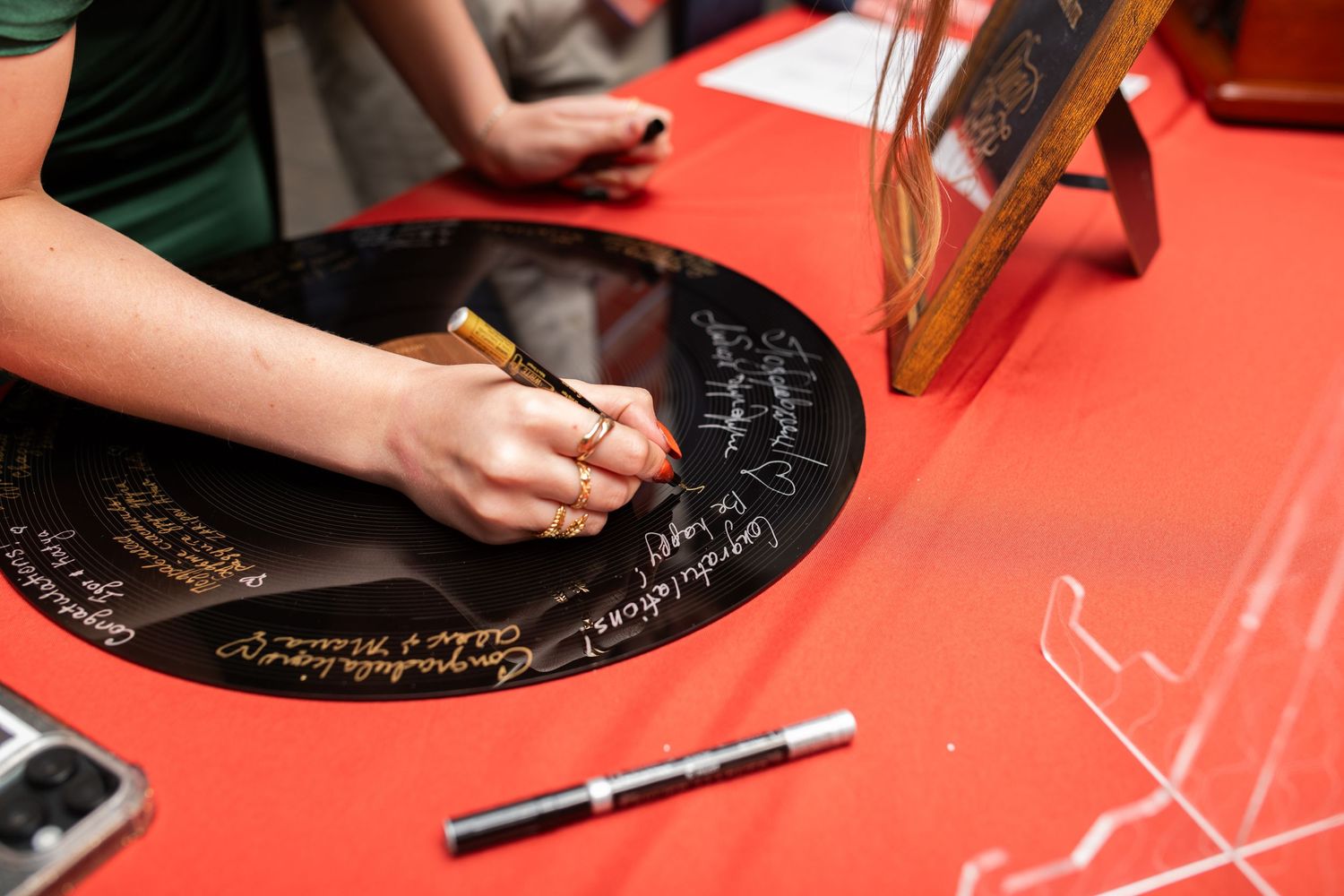 Guest signing vinyl record as alternative wedding guestbook on red tablecloth.