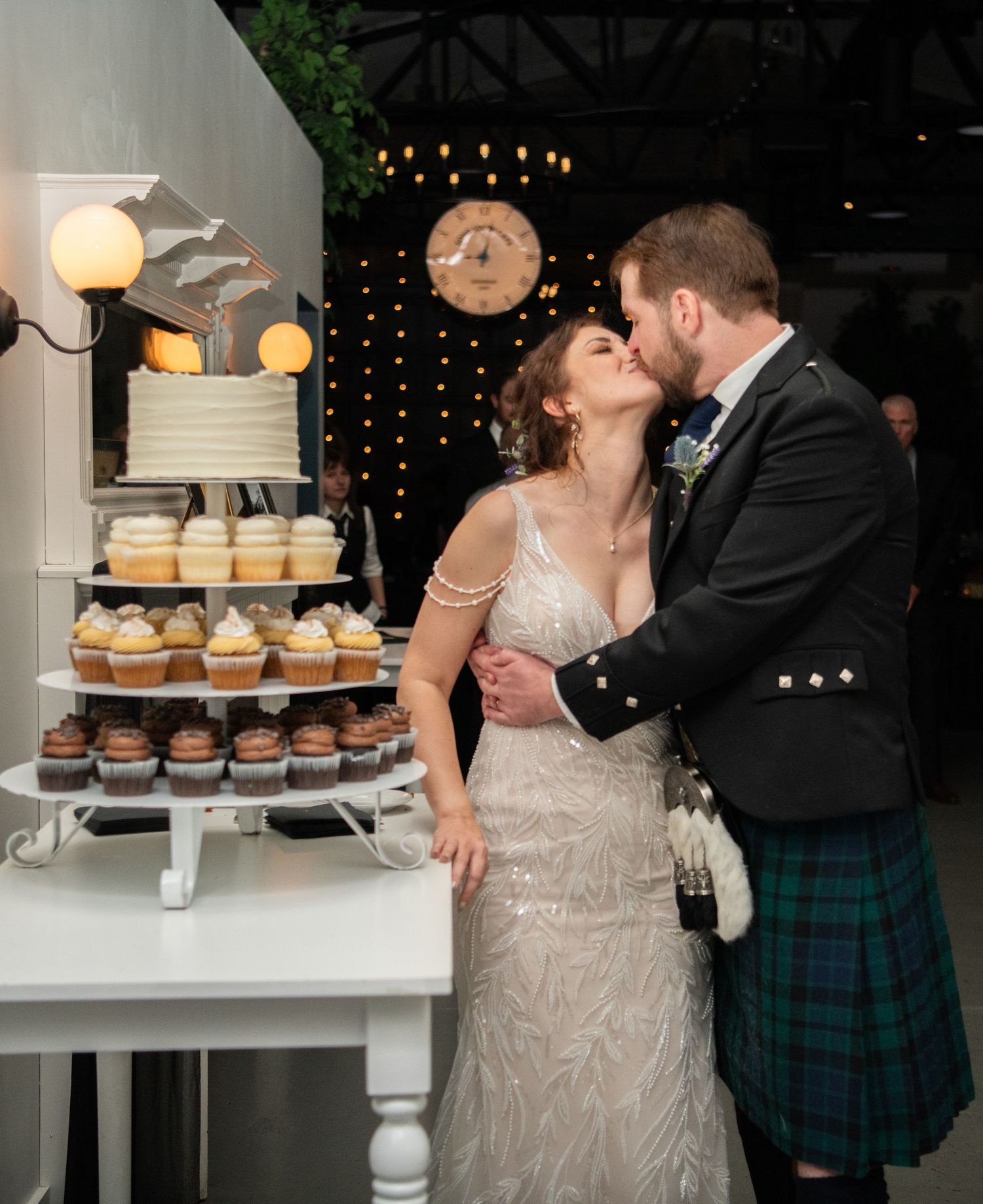 Couple kissing by tiered cupcake display at wedding reception.