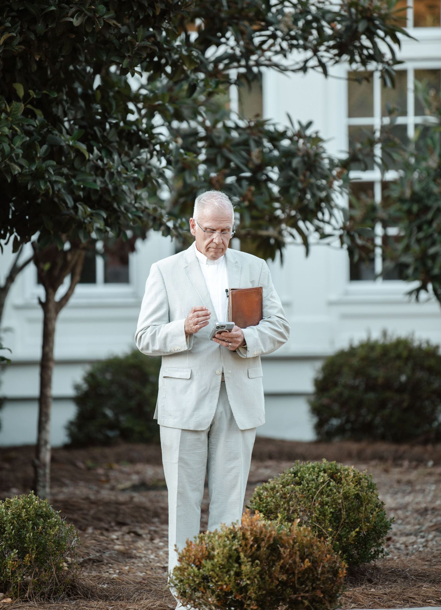 Person in white suit reading from a small book outdoors.