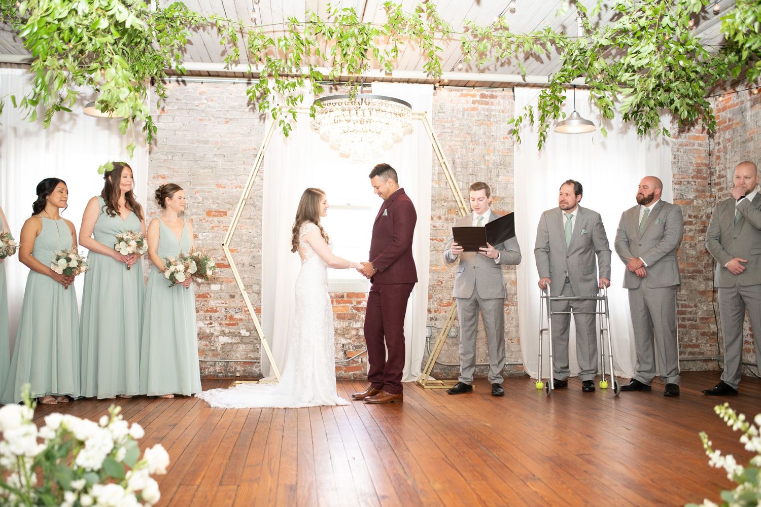 Wedding ceremony setup in a light-filled venue with brick walls and botanical decorations.